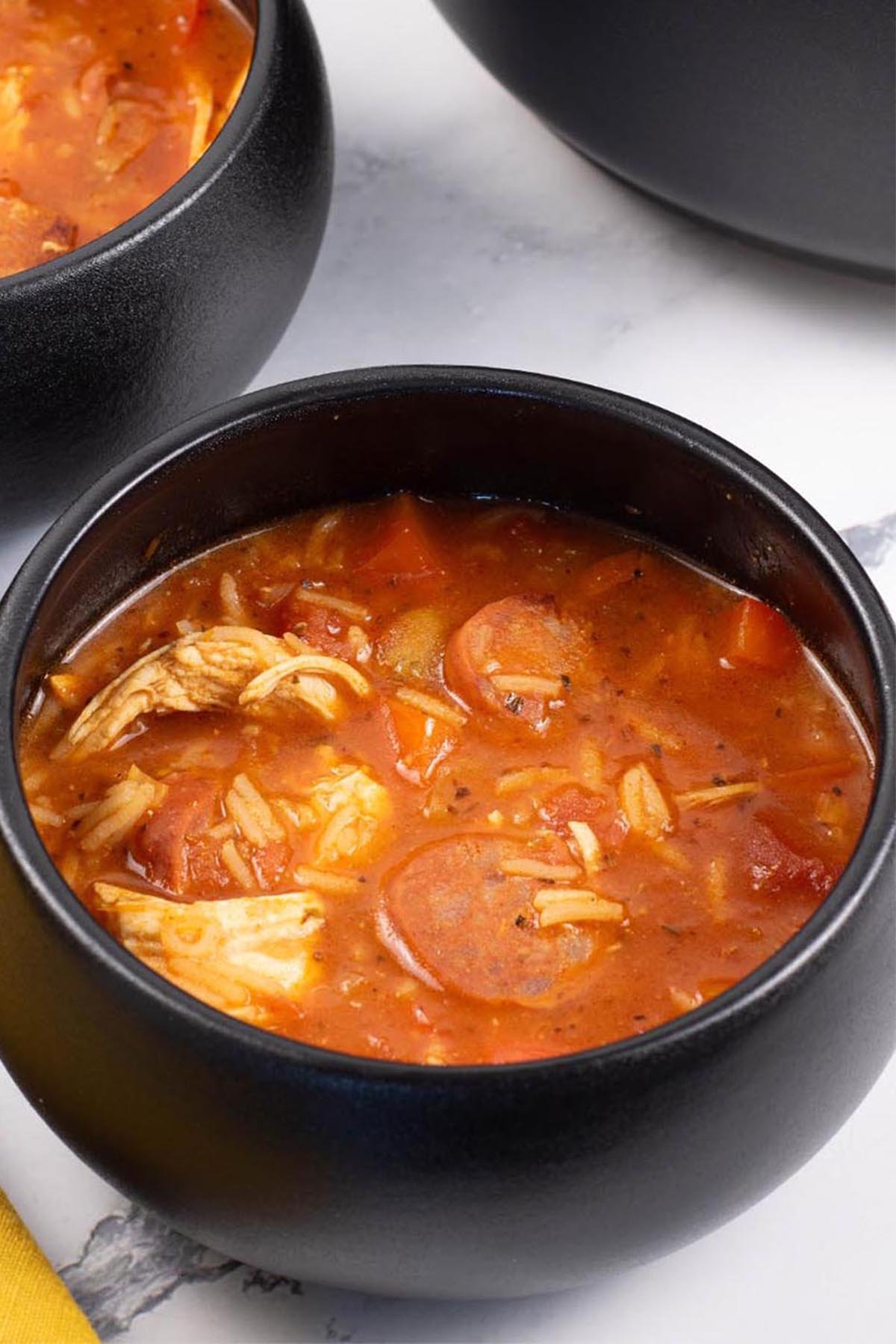 Two portions of Spanish chicken, chorizo and rice soup in black bowls.