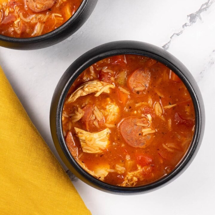 Two portions of Spanish chicken, chorizo and rice soup in black bowls.
