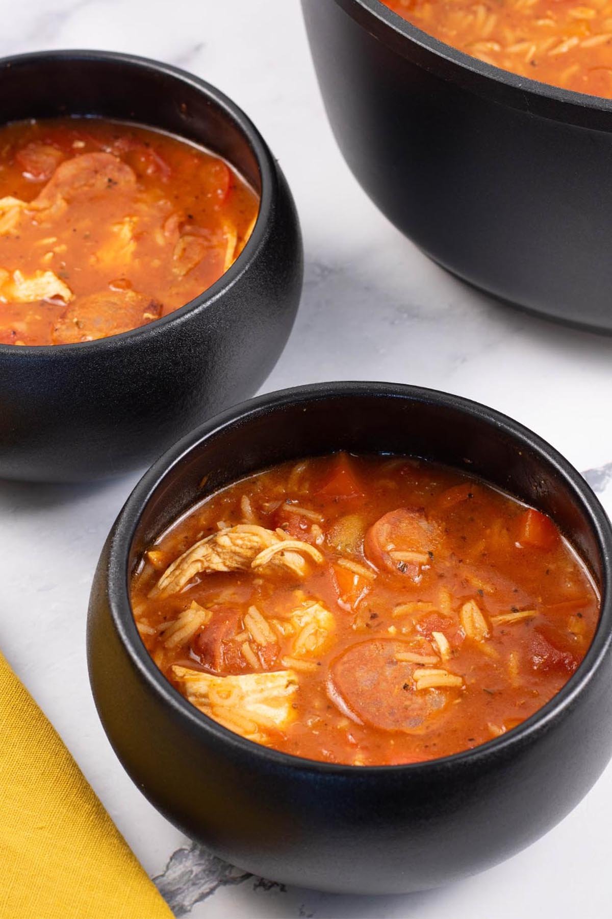 Two portions of Spanish chicken, chorizo and rice soup in black bowls.
