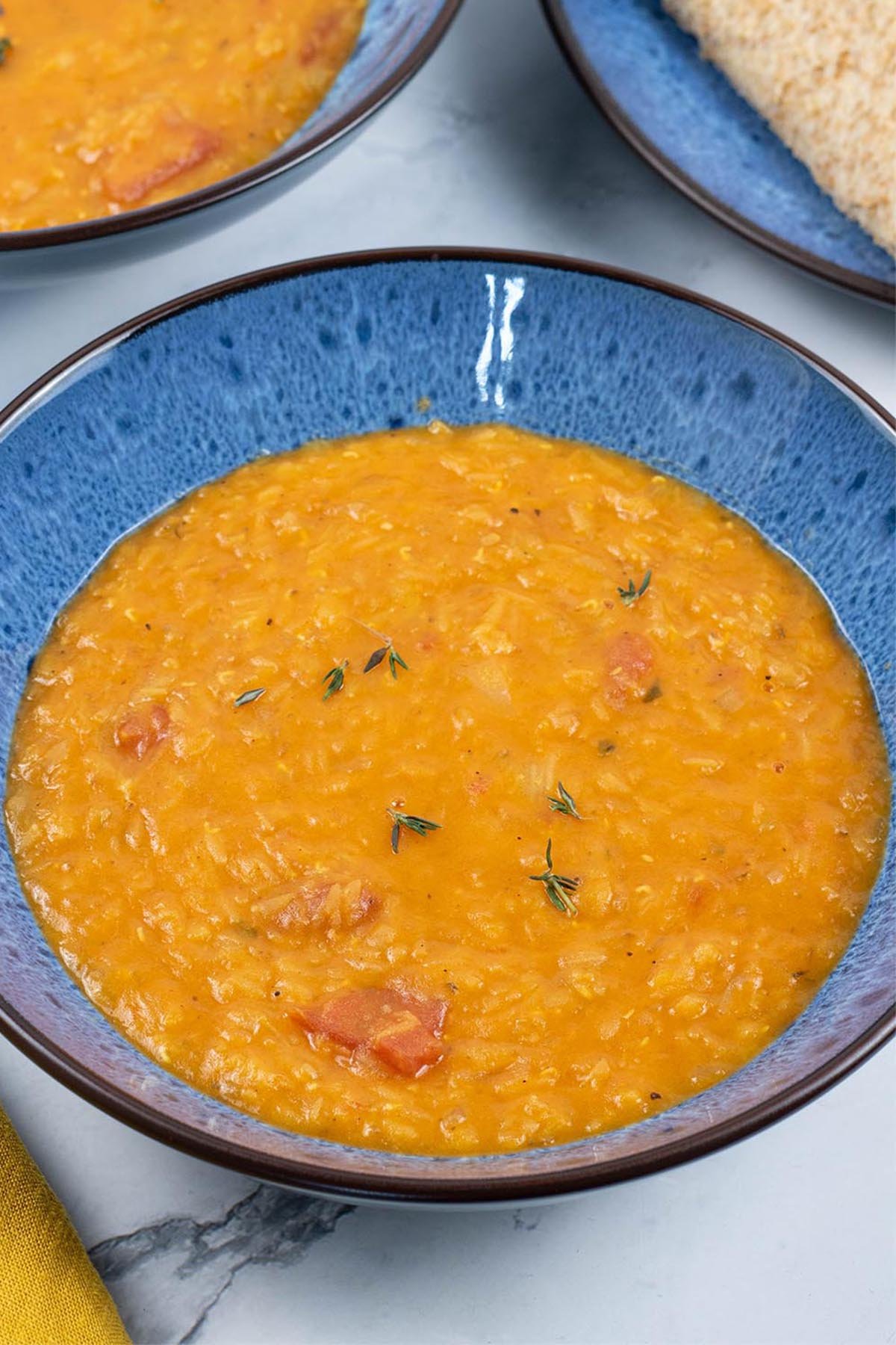 Two portions of tomato, lentil and thyme soup, made in the Thermomix, in blue patterned bowls with a plate of sliced brown bread on the side.