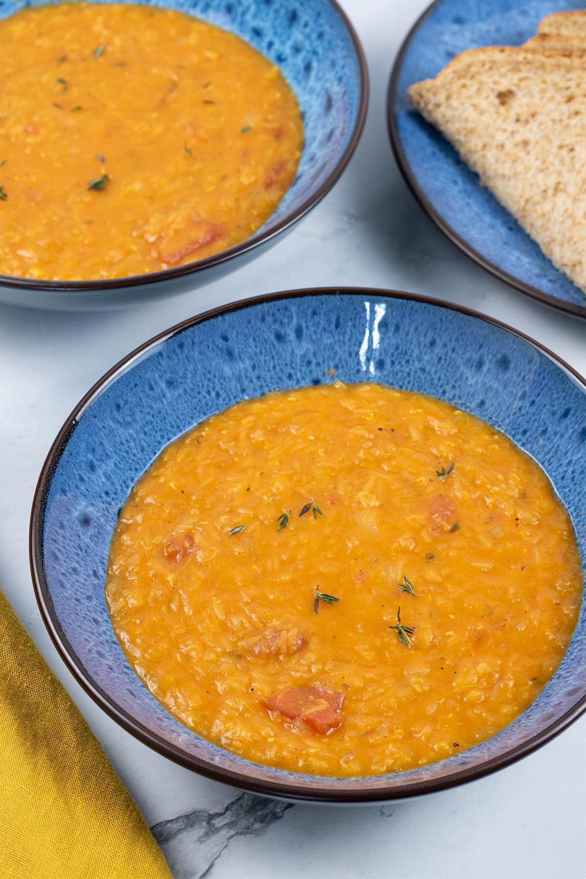 Two portions of tomato, lentil and thyme soup, made in the Thermomix, in blue patterned bowls with a plate of sliced brown bread on the side.