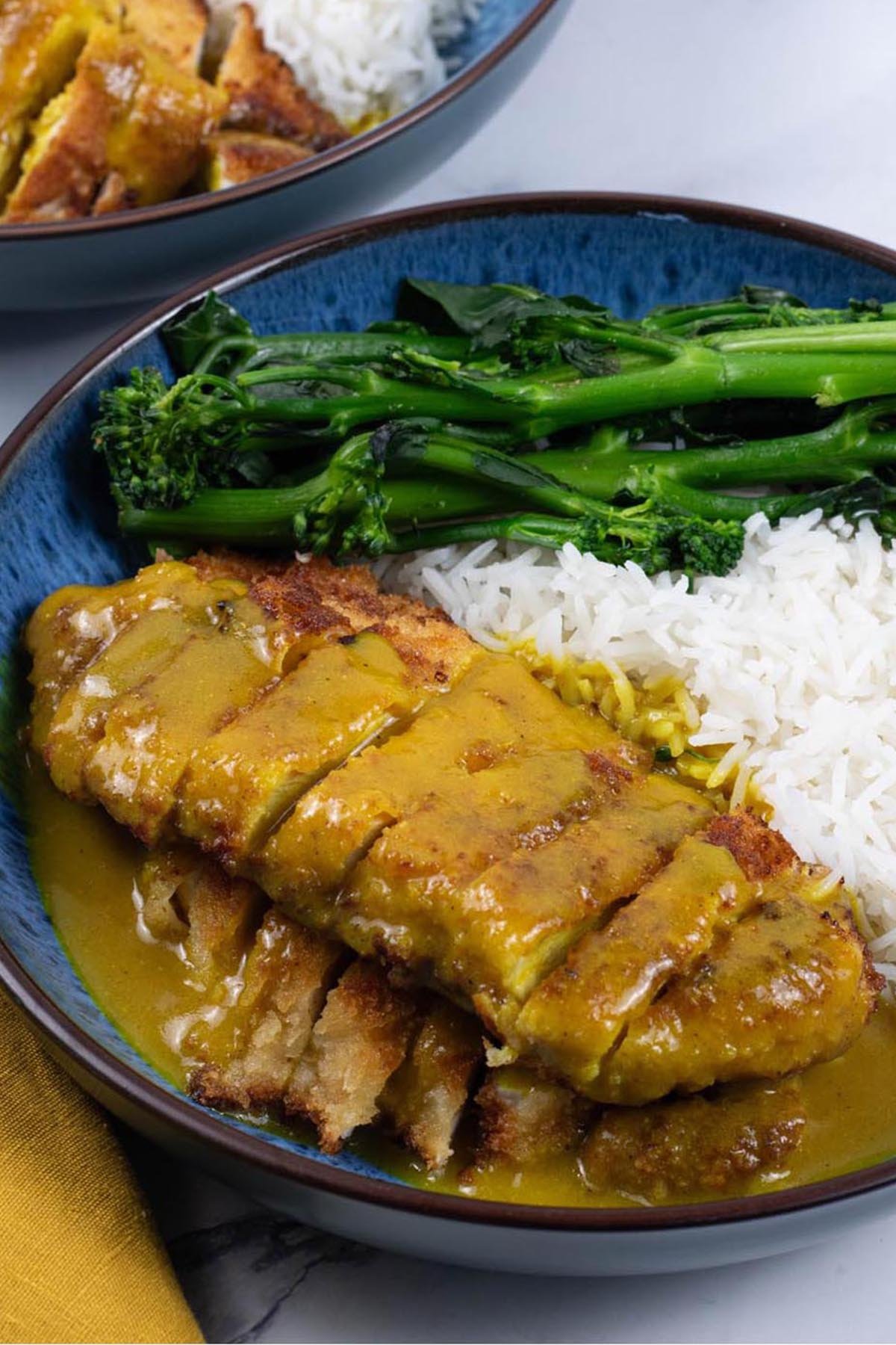 Two portions of Wagamama chicken katsu curry in blue patterned bowls with basmati rice and tenderstem broccoli.