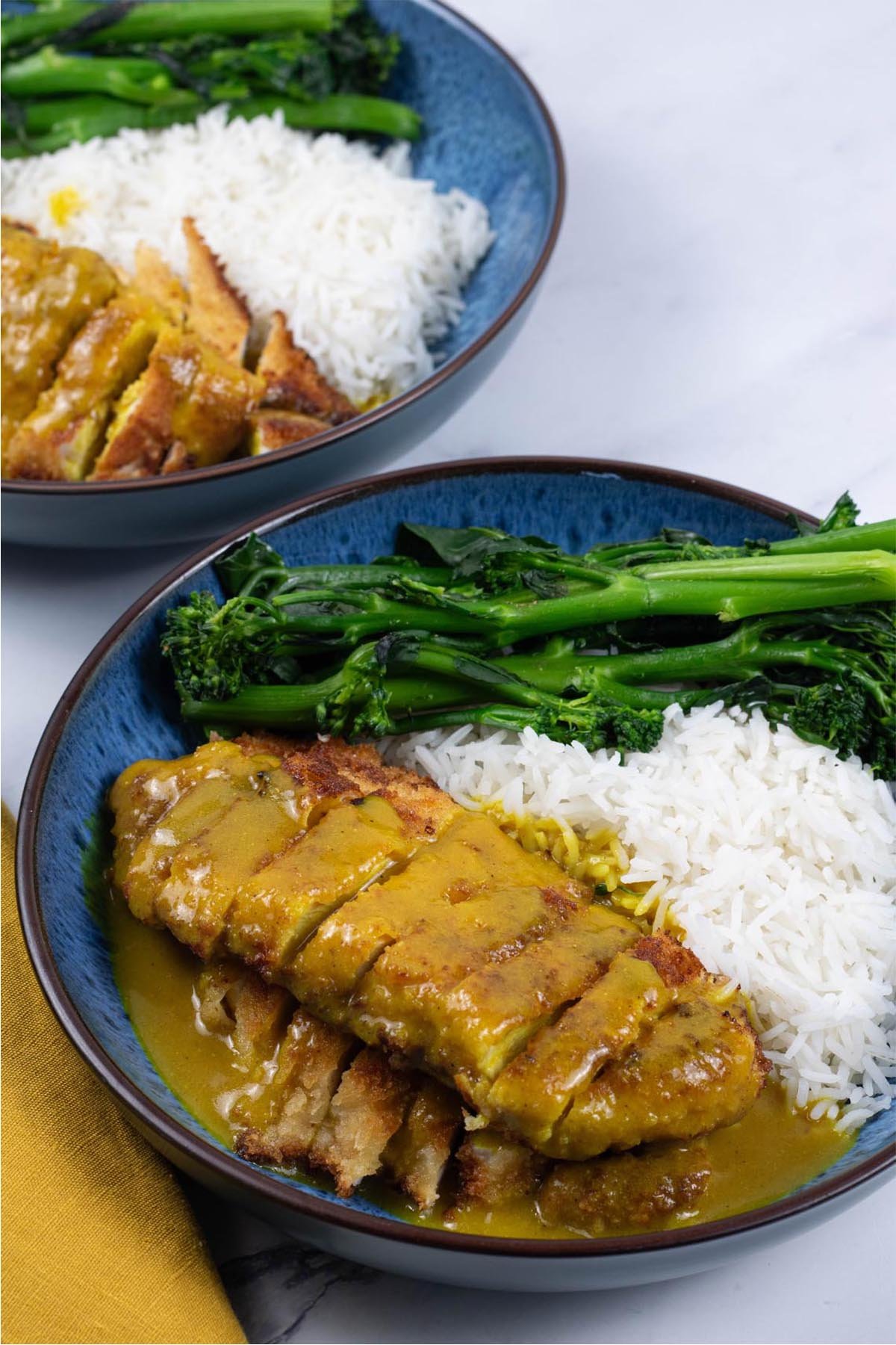 Two portions of Wagamama chicken katsu curry in blue patterned bowls with basmati rice and tenderstem broccoli.