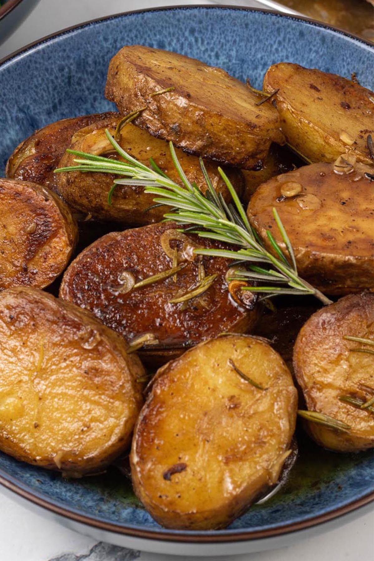 Close up of buttery herbed melting potatoes in a blue patterned serving bowl.