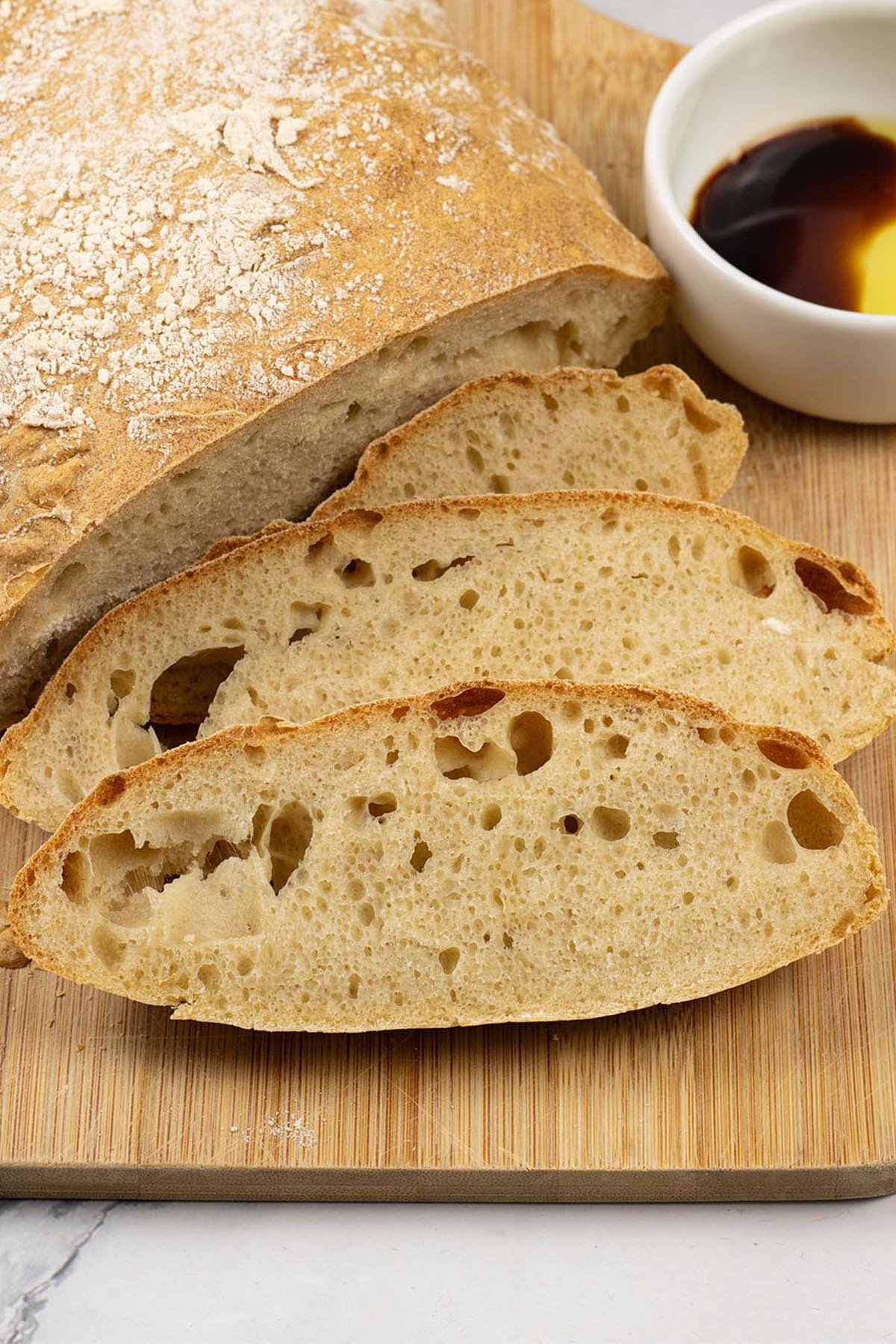 Ciabatta bread on a board with 3 pieces sliced and a small dish of extra virgin olive oil and balsamic vinegar.