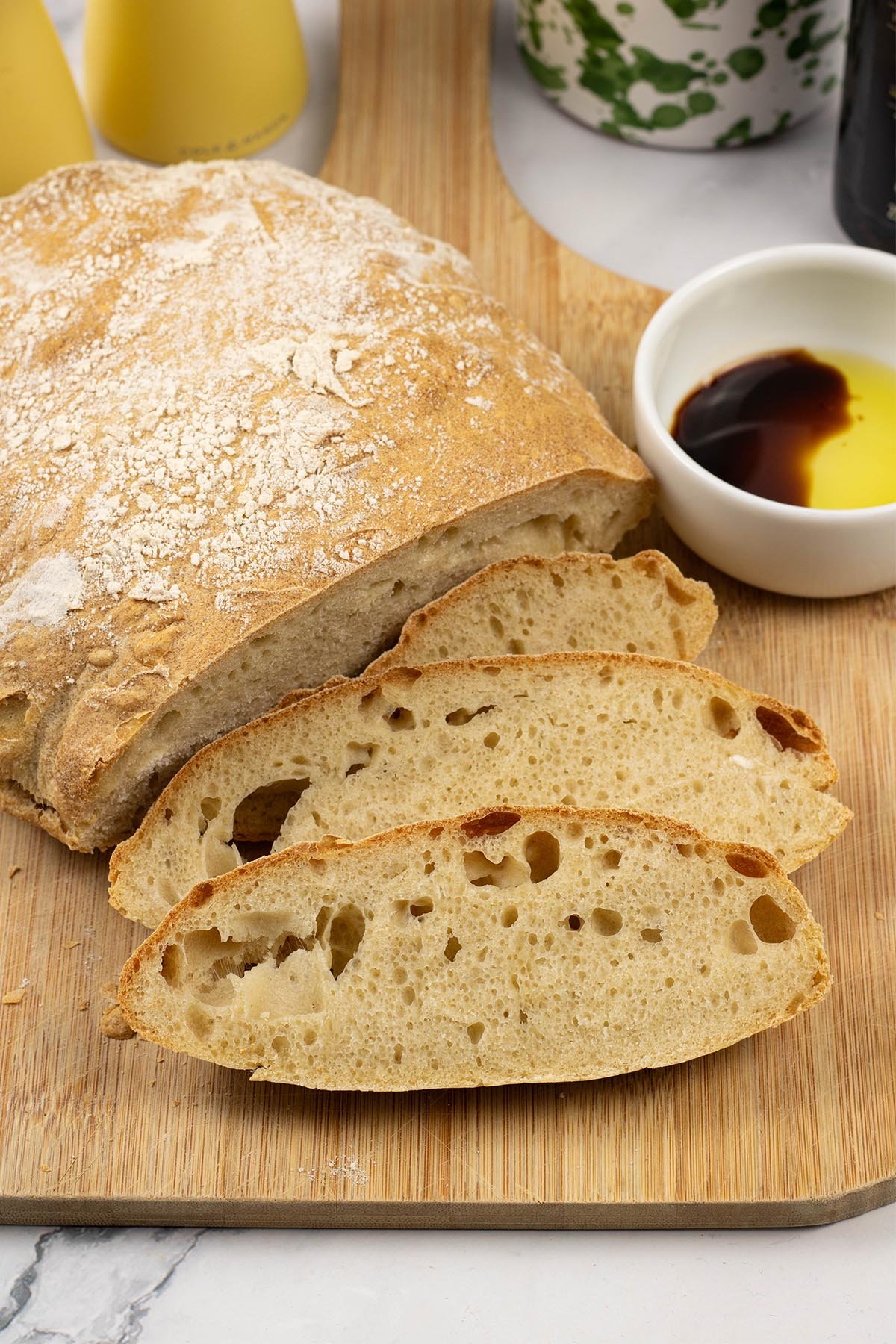Ciabatta bread on a board with 3 pieces sliced and a small dish of extra virgin olive oil and balsamic vinegar.