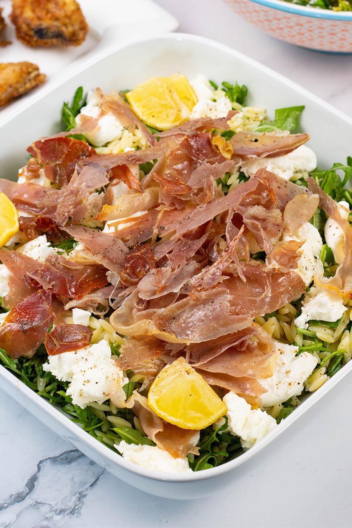Crispy prosciutto and orzo salad in a white square serving dish.
