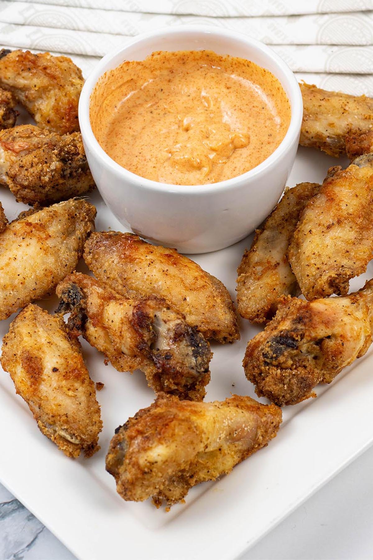 Easy air fryer cajun chicken wings on a white square platter with a dish of cajun dipping sauce and paper napkins on the side.
