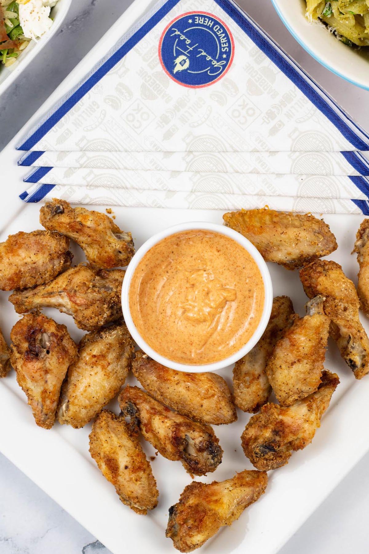 Easy air fryer cajun chicken wings on a white square platter with a dish of cajun dipping sauce and paper napkins on the side.