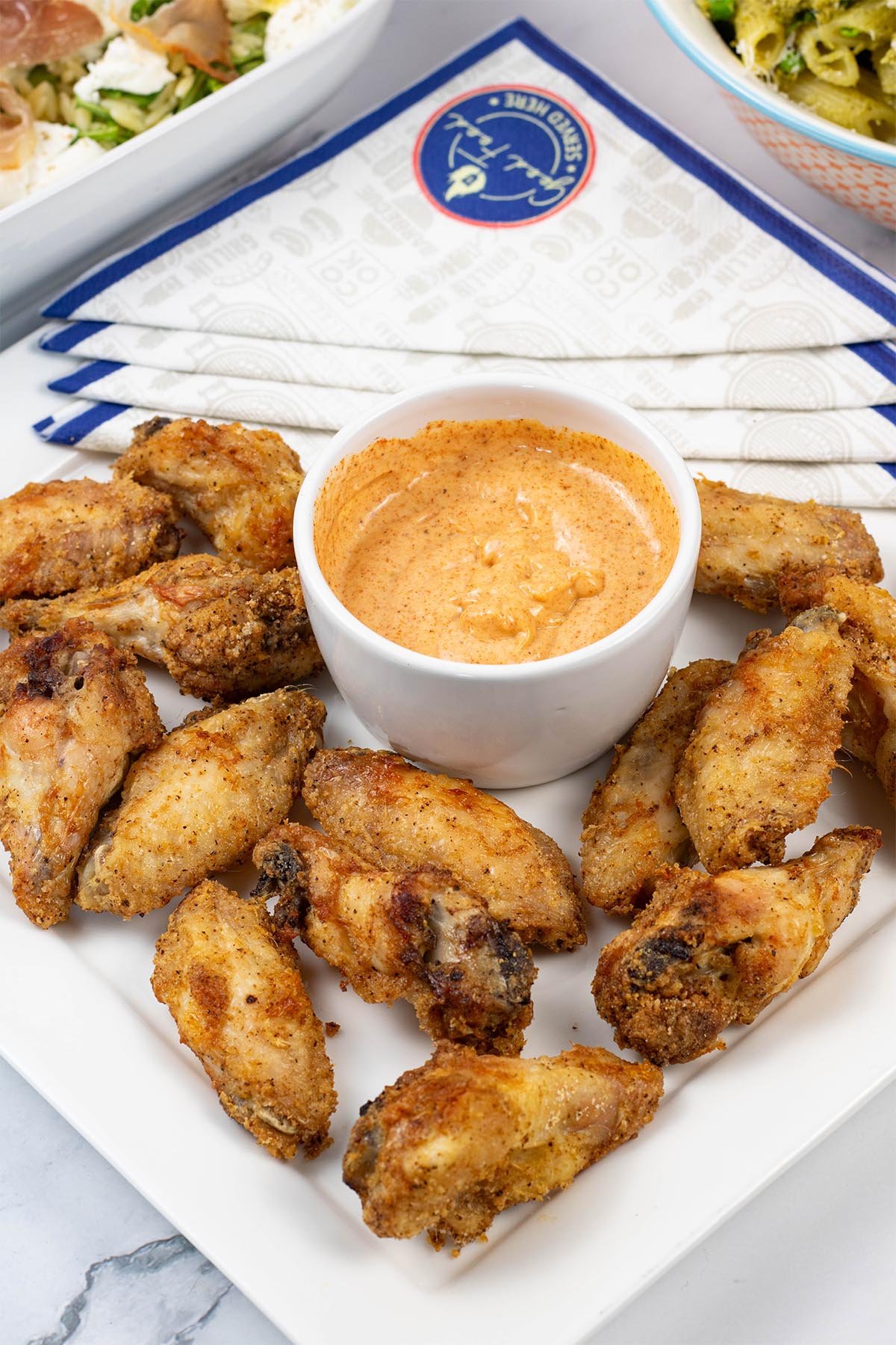 Easy air fryer cajun chicken wings on a white square platter with a dish of cajun dipping sauce and paper napkins on the side.
