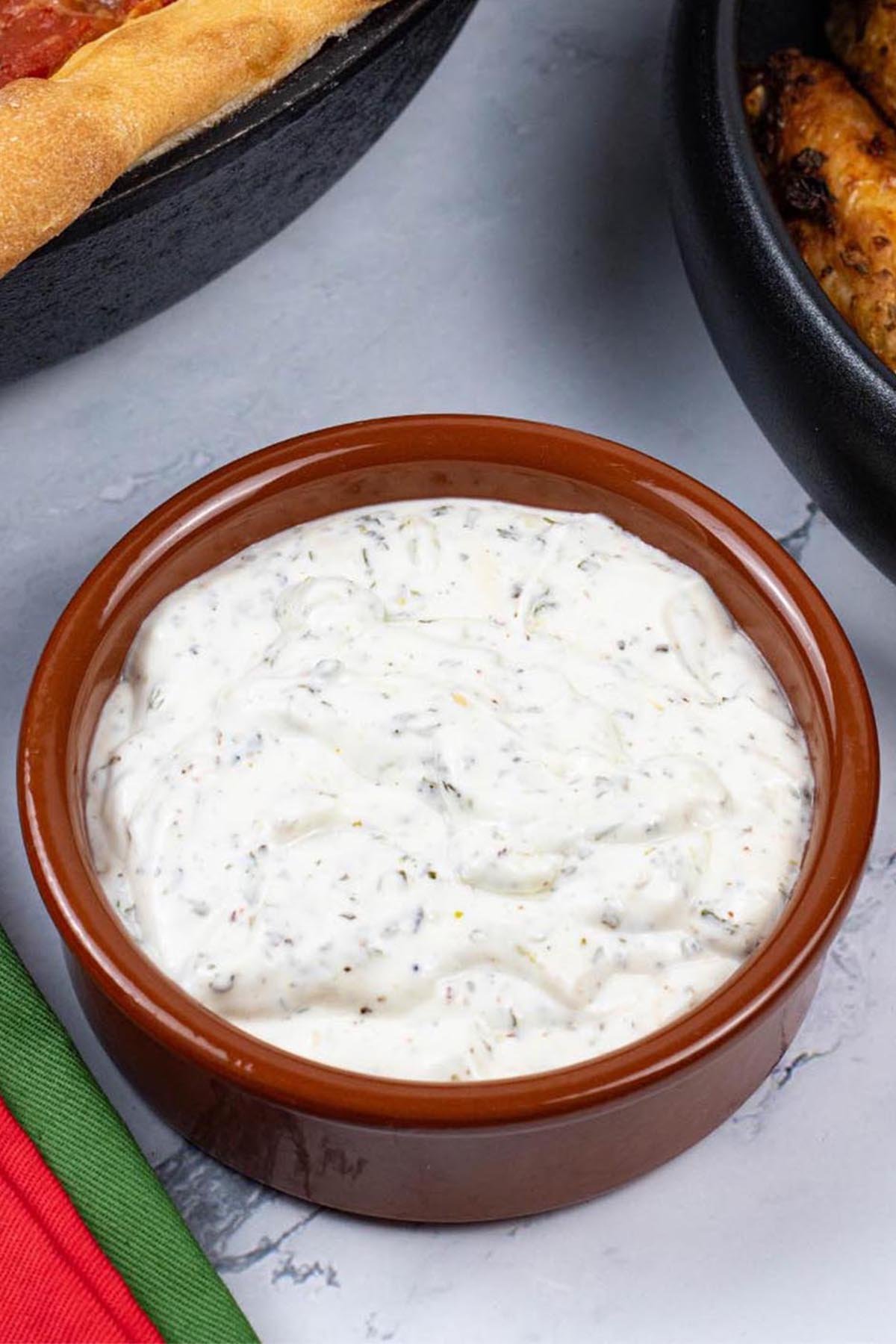Garlic and herb dip in a small round terracotta dish with a Chicago deep pan pizza and easy air fryer Spanish chicken wings on the side.