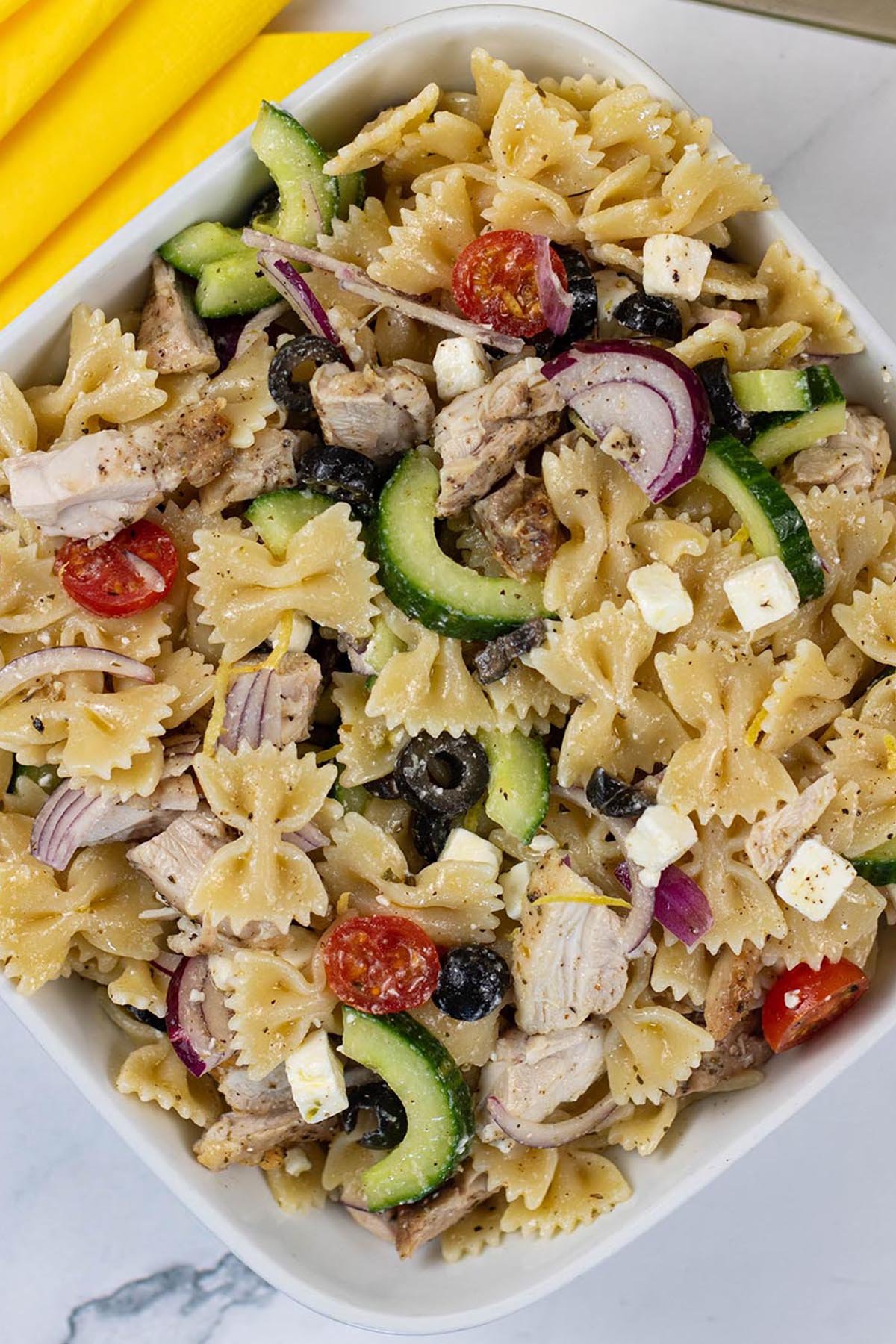 Greek chicken pasta salad in a square white serving dish with yellow napkins on the side.