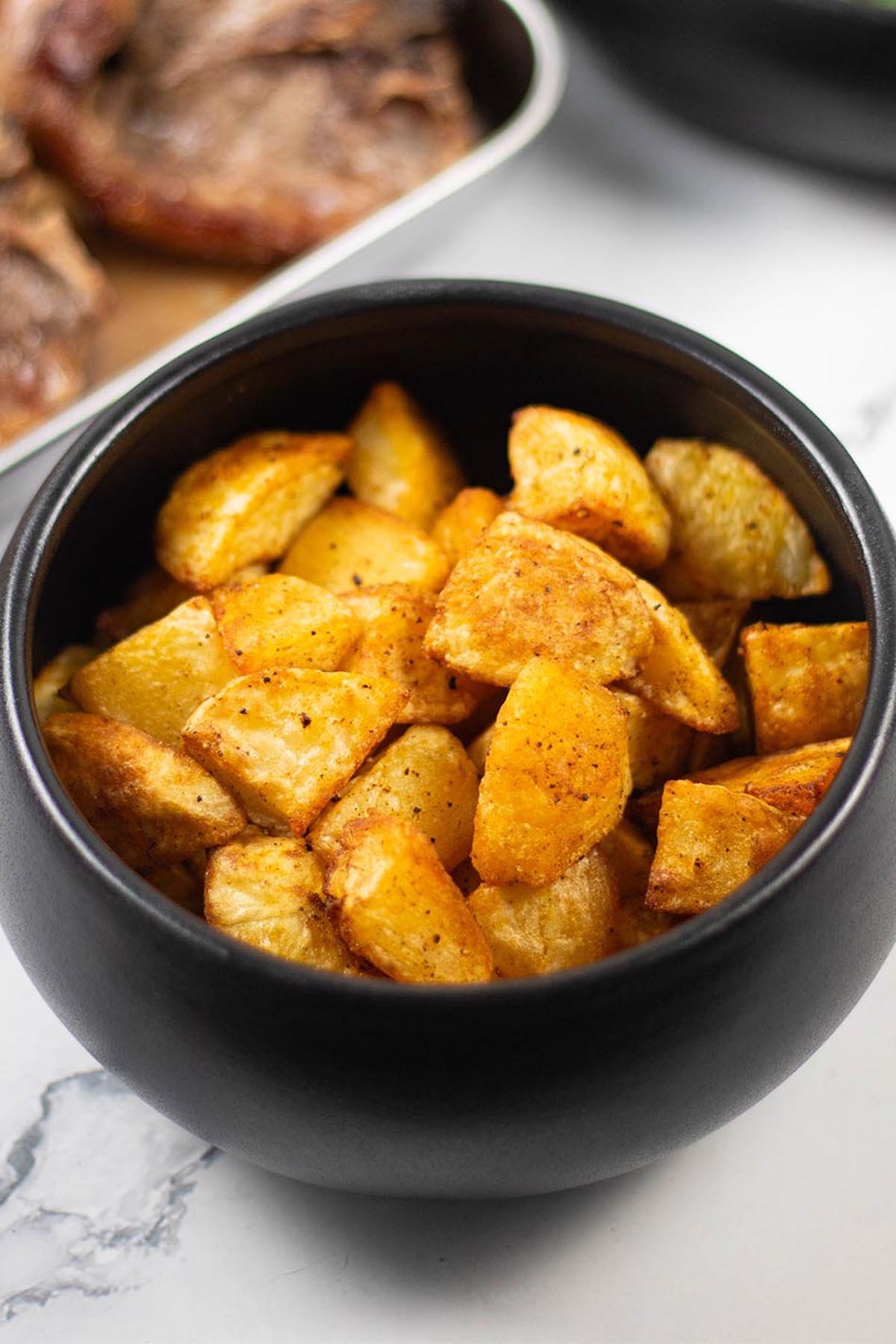 Paprika parmentier potatoes in a black serving bowl with pan-fried lamb chops in the background.