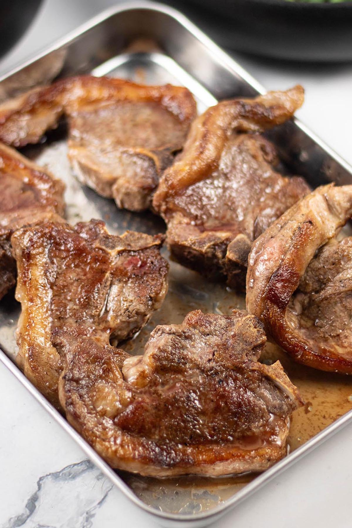 6 perfect pan-fried lamb chops resting on a tray.