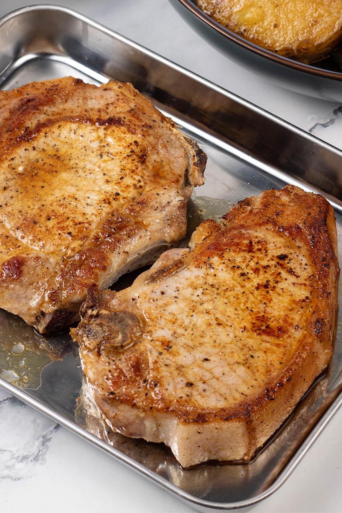 2 perfect pan-fried pork chops resting on a tray.