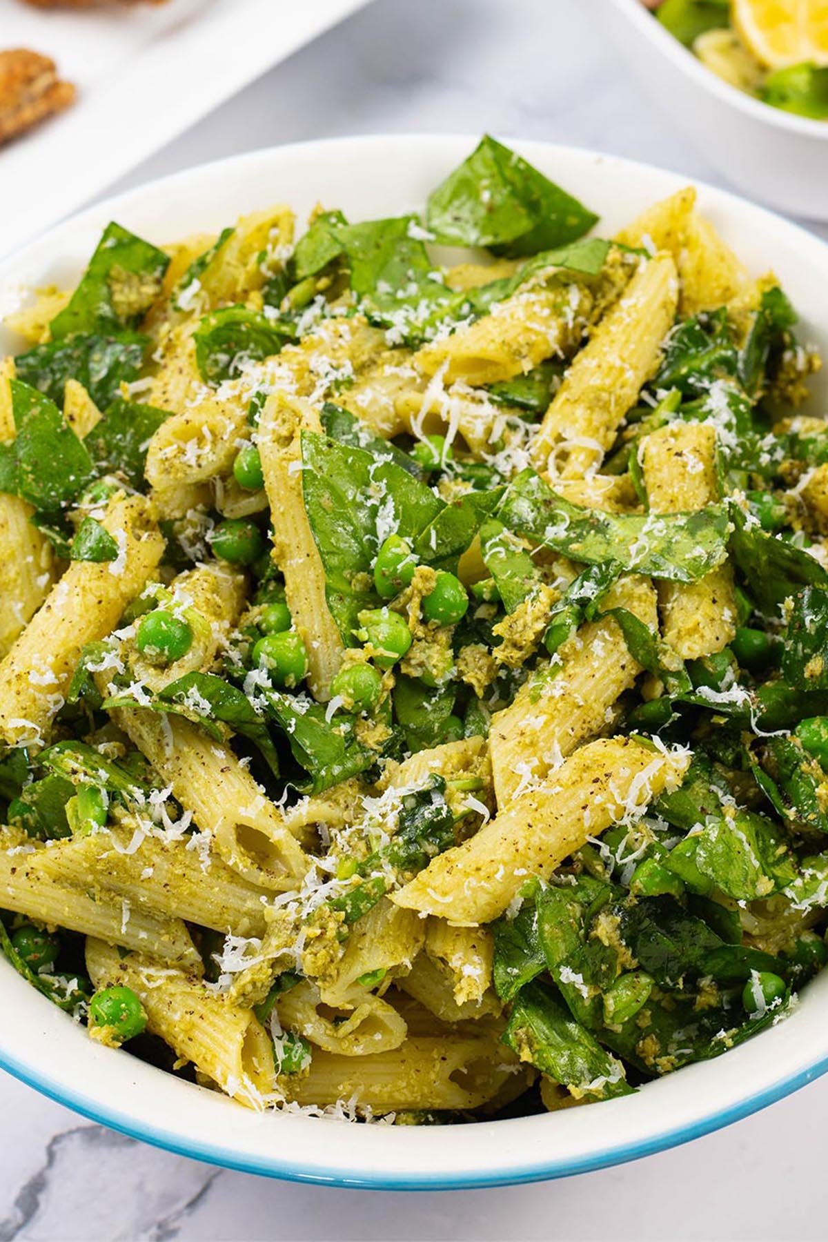 Pesto, peas and spinach pasta salad in a light blue trimmed serving bowl.