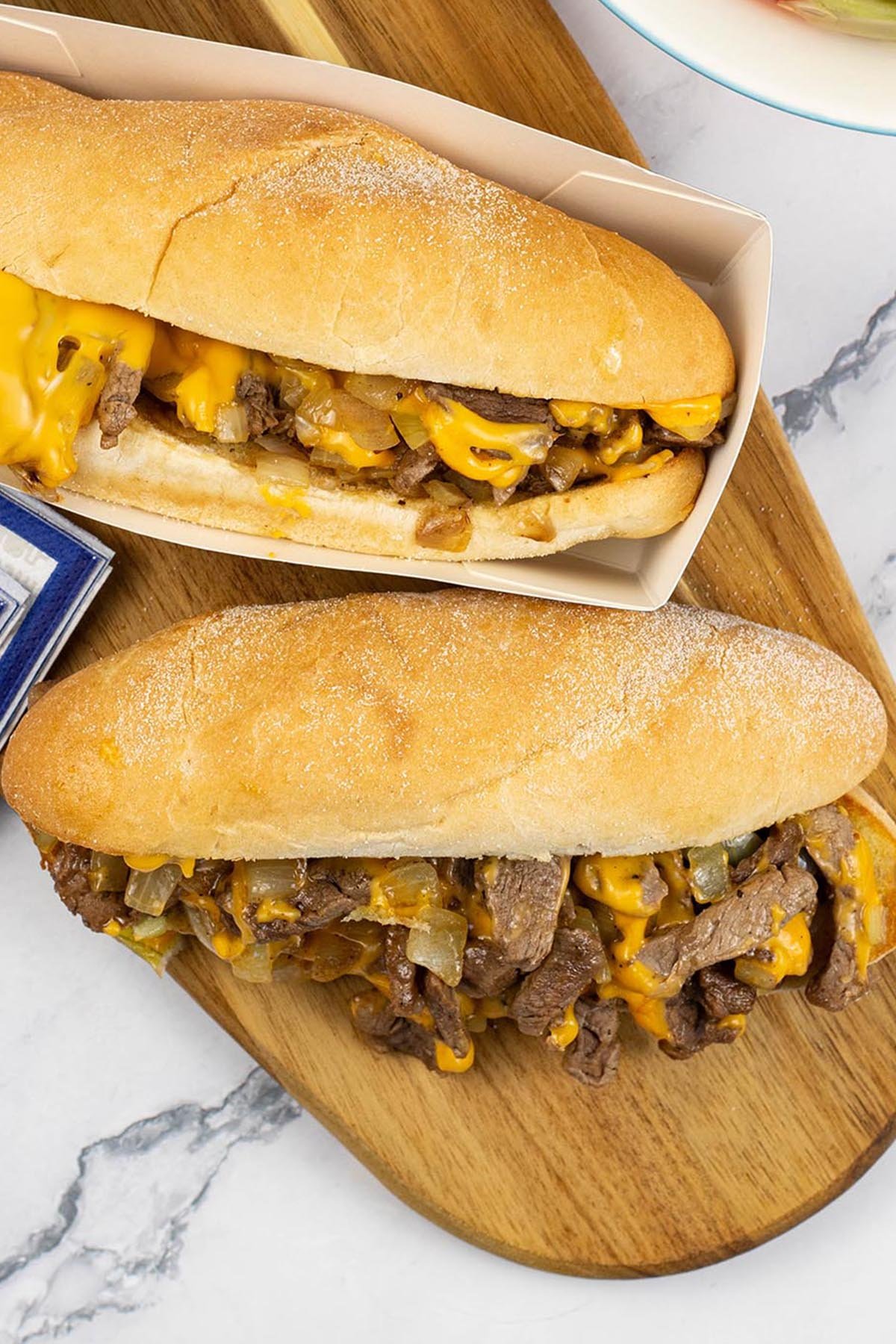 Close up of two Philly cheesesteaks on a wooden board.