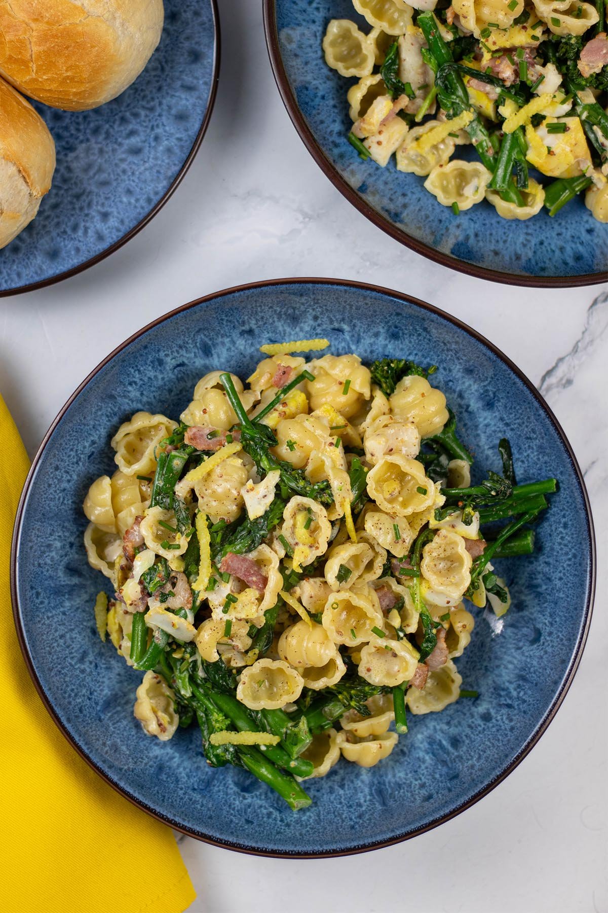 Two portions of smoked haddock with tenderstem broccoli, spinach and conchiglie in blue patterned bowls with a plate of crusty bread on the side.