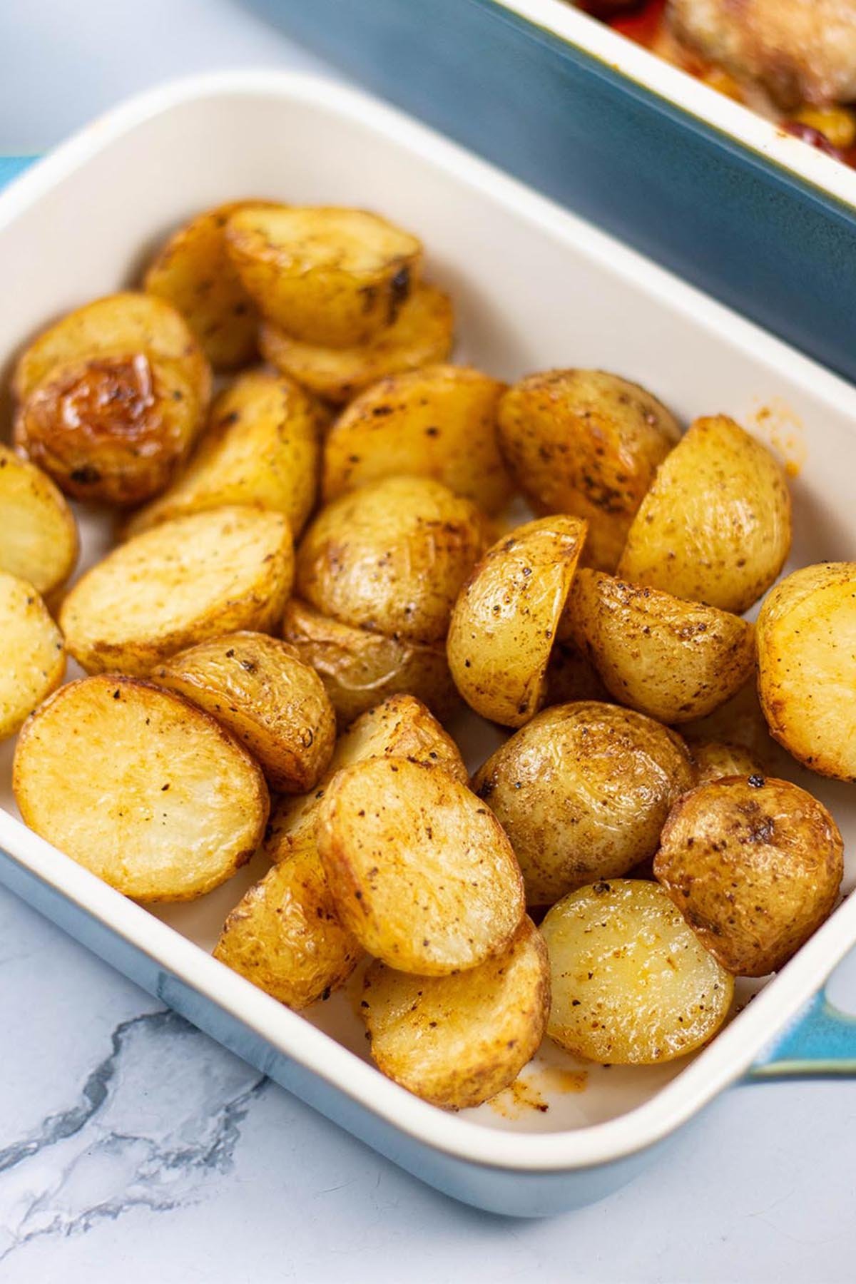 Spanish-style roast baby potatoes in a small rectangle Staub oven dish, with a large dish of Spanish chicken traybake in the background.