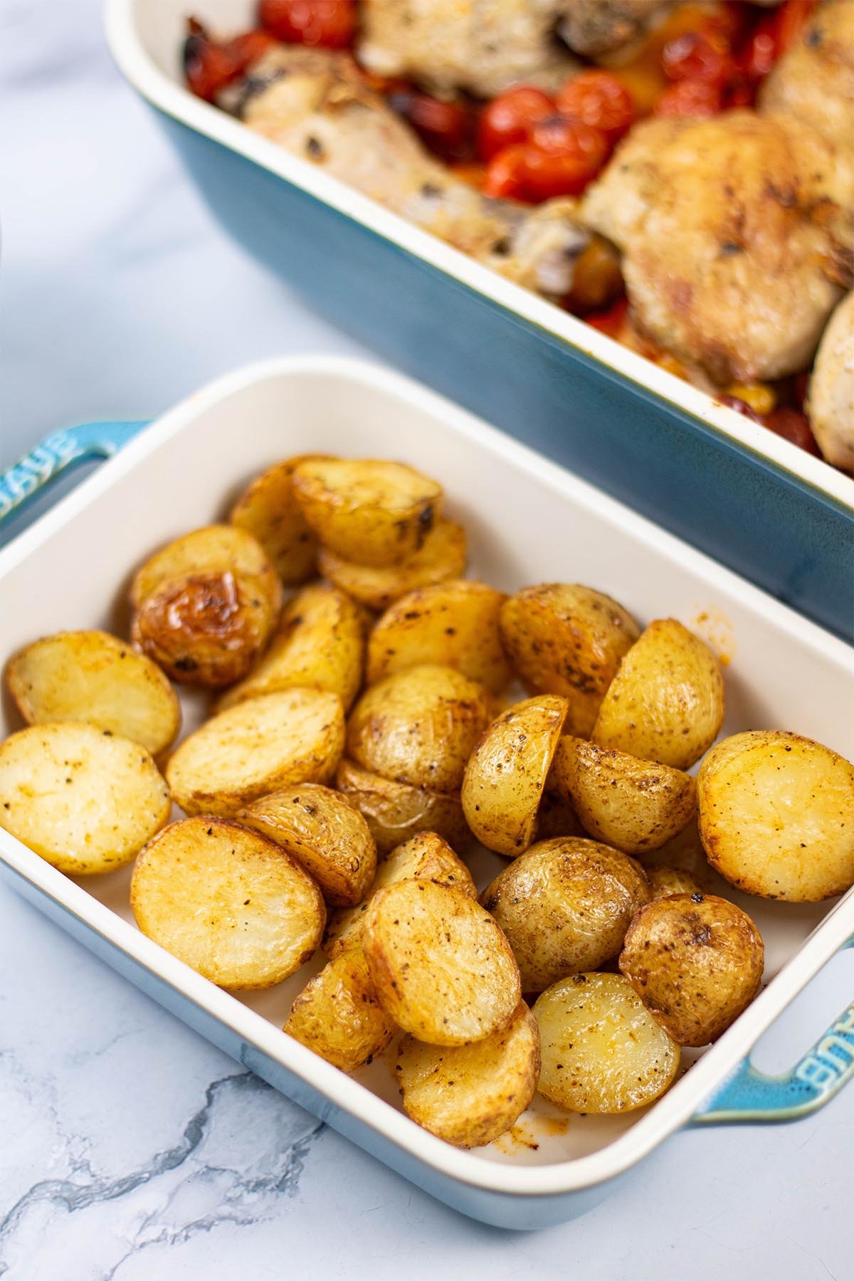 Spanish-style roast baby potatoes in a small rectangle Staub oven dish, with a large dish of Spanish chicken traybake in the background.