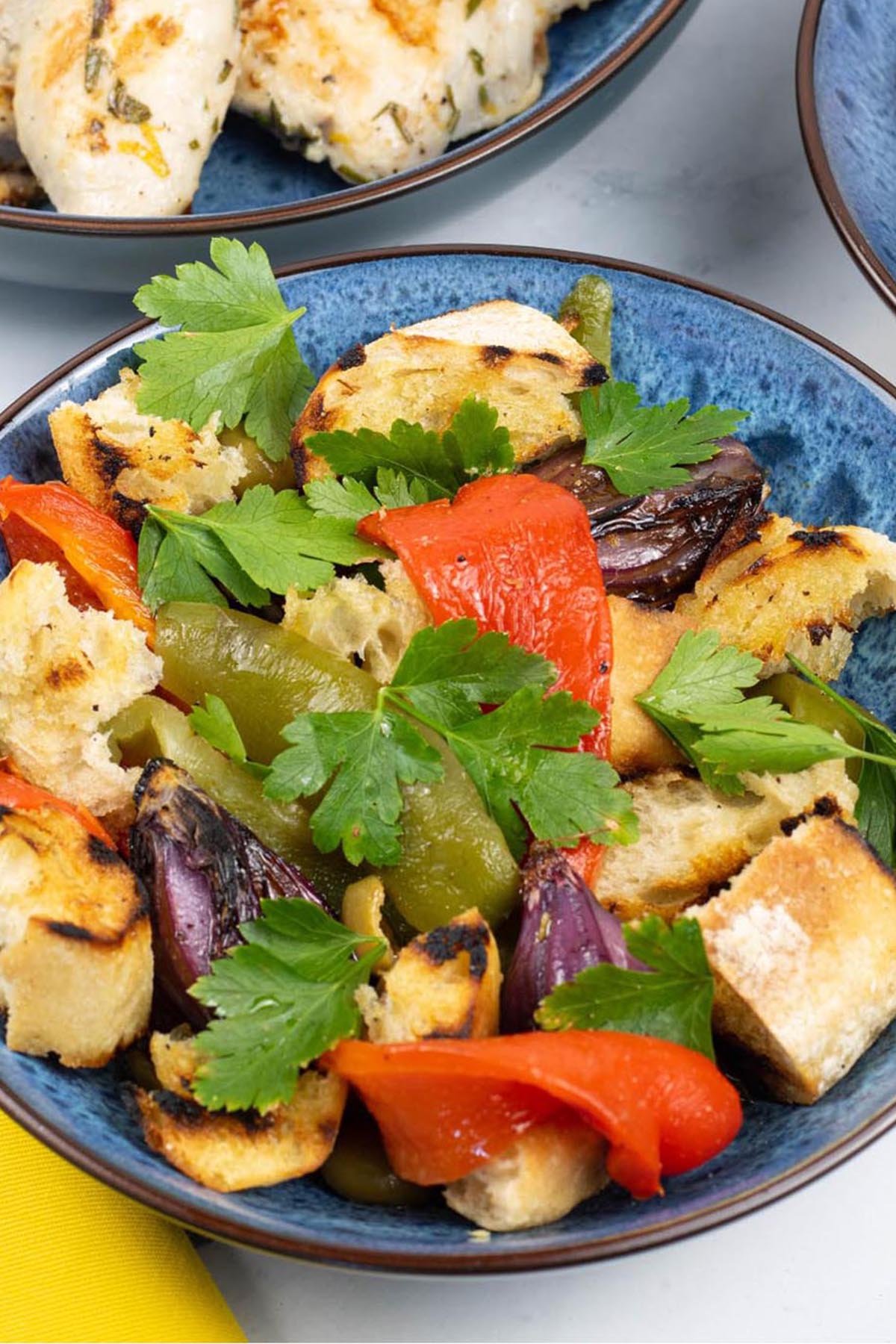 Barbecued mixed pepper salad for 2 in a blue patterned bowl with a dish of lemon herb chicken thighs on the side.