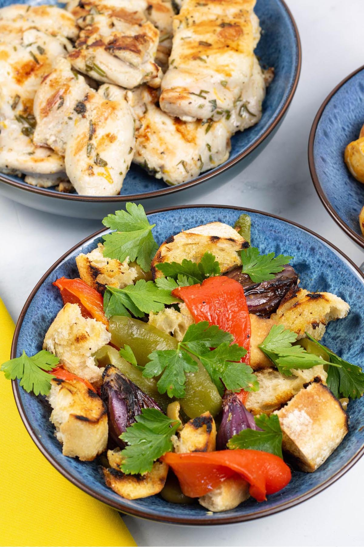 Barbecued mixed pepper salad for 2 in a blue patterned bowl with a dish of lemon herb chicken thighs on the side.