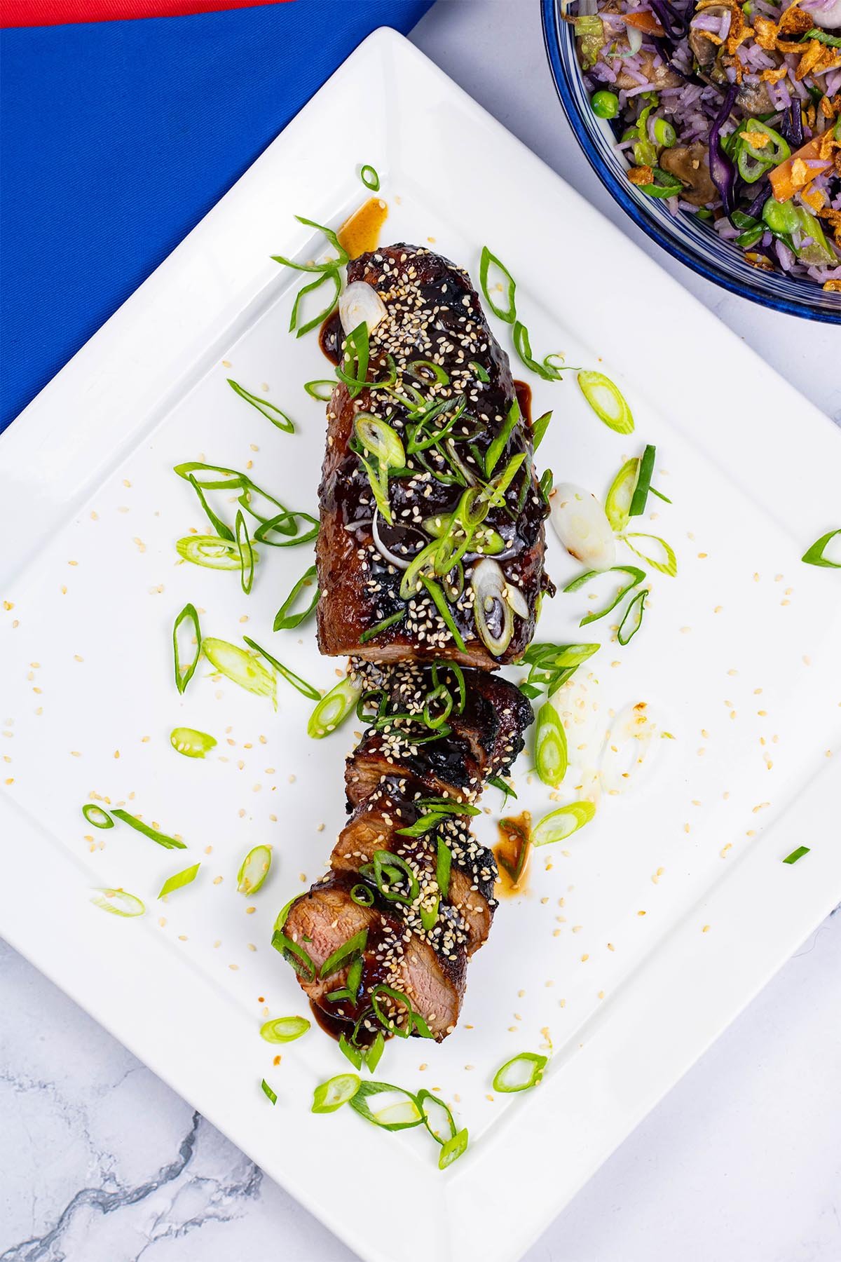 Korean barbecued pork fillet sliced and garnished with spring onions on a square white platter.