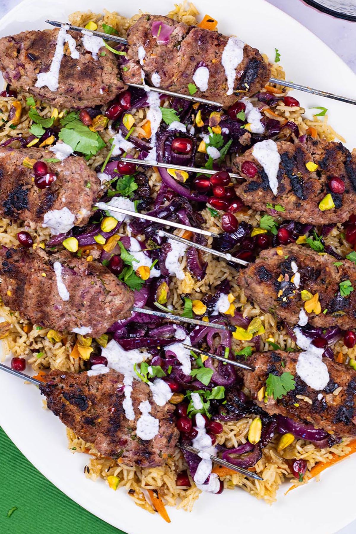 Lamb koftas with jewelled rice on an oval white platter with a green napkin on the side.
