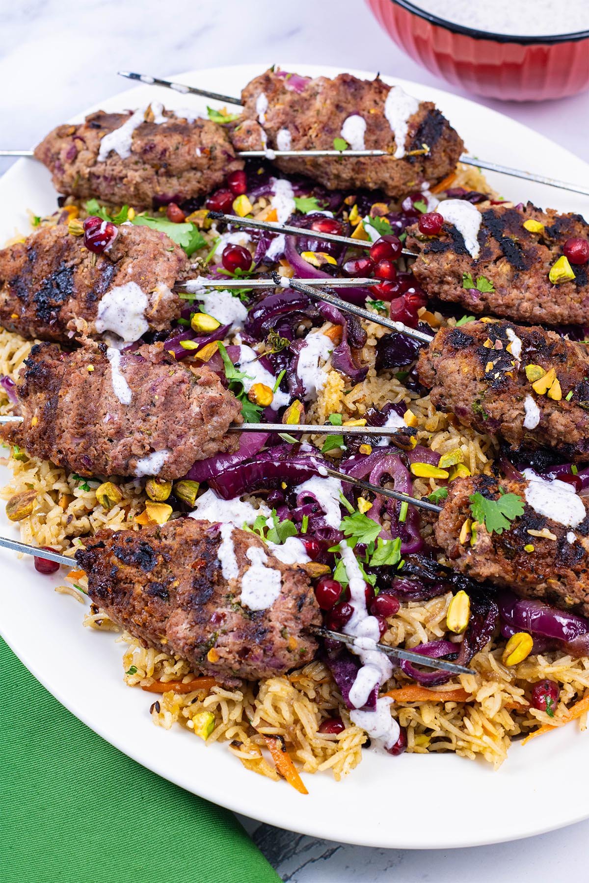 Lamb koftas with jewelled rice on an oval white platter with a green napkin on the side.
