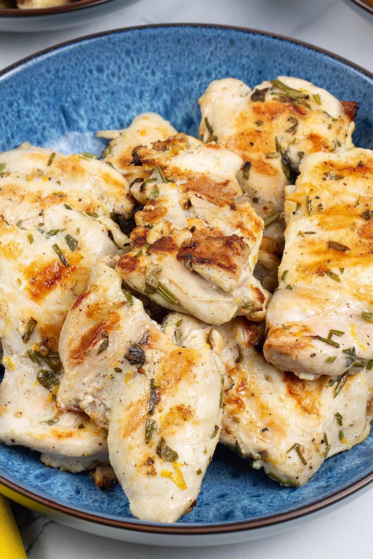 Close up of lemon herb chicken thighs in a blue patterned serving bowl.