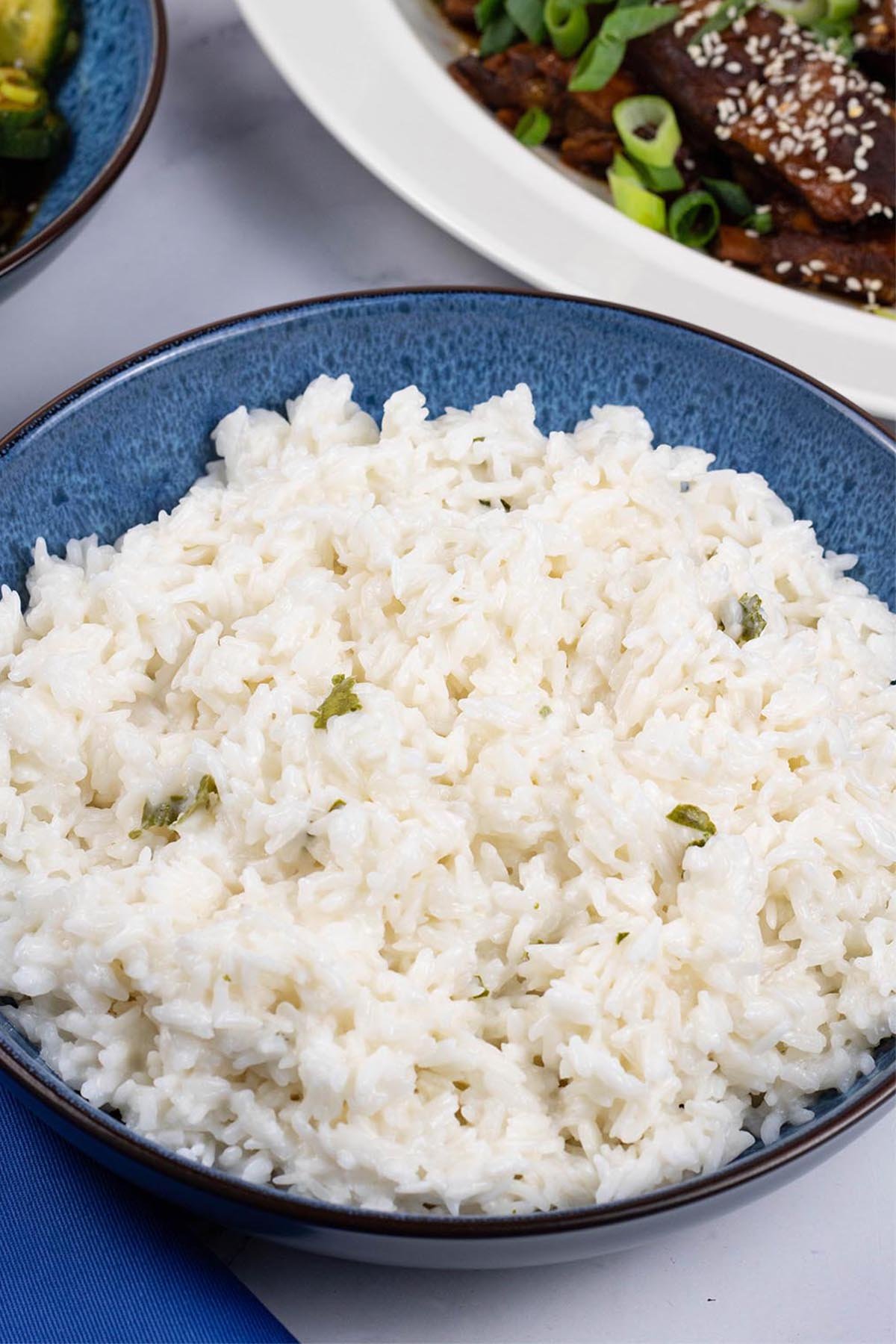 Coconut rice in a blue patterned serving bowl with a platter of slow cooker gochujang pork ribs in the background.