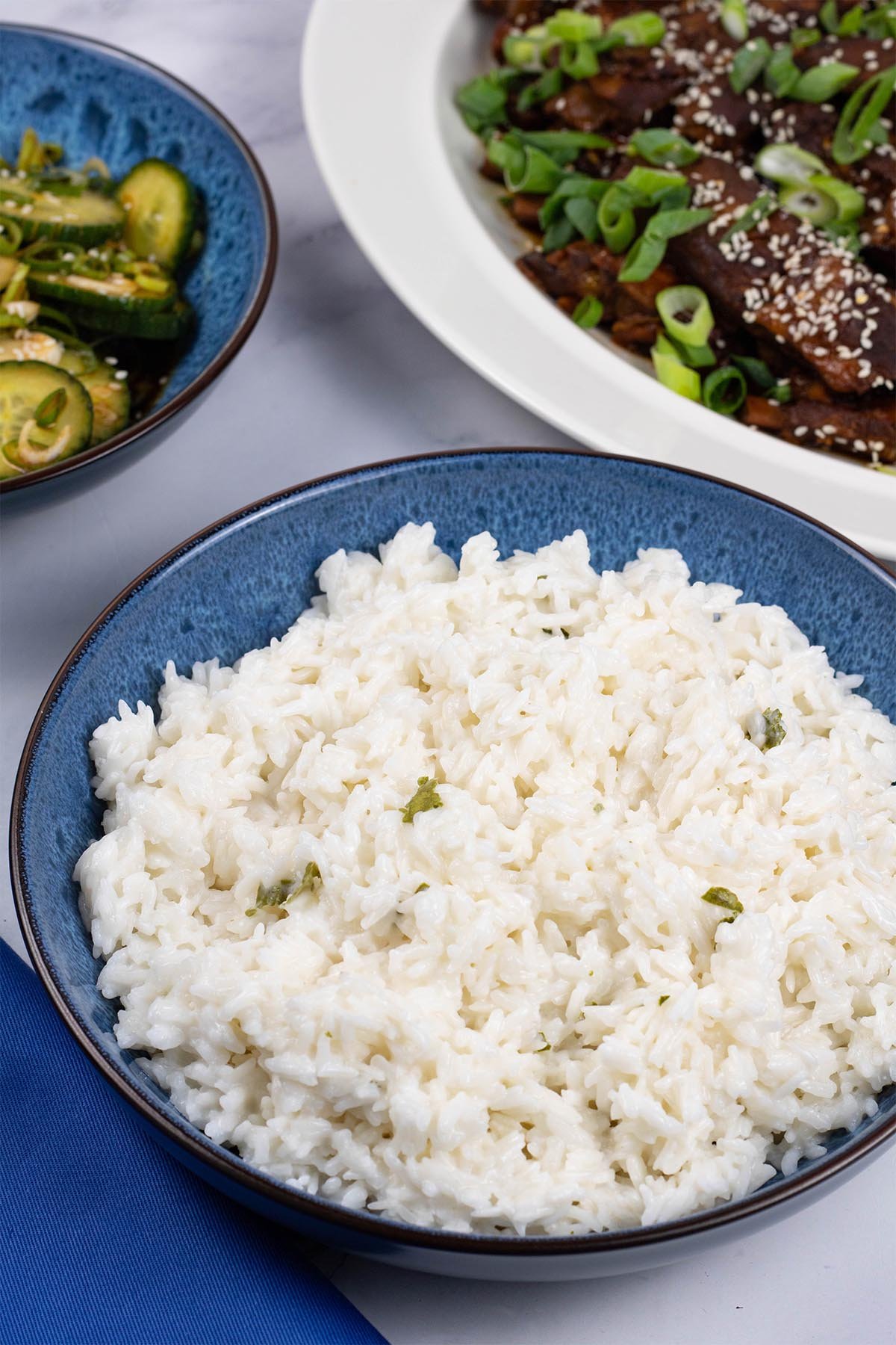 Coconut rice in a blue patterned serving bowl with a platter of slow cooker gochujang pork ribs in the background.