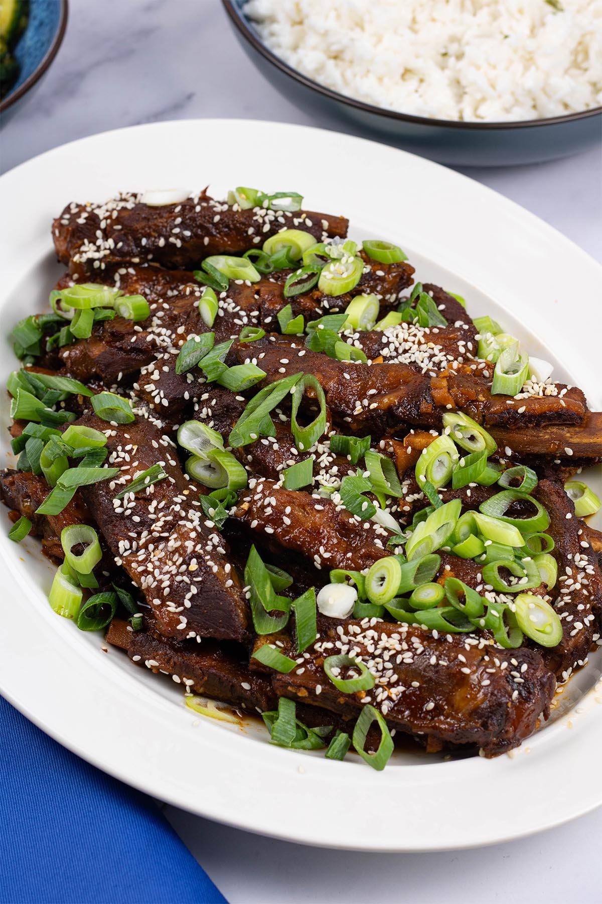 Slow cooker gochujang pork ribs on an oval white platter with a bowl of coconut rice in the background.