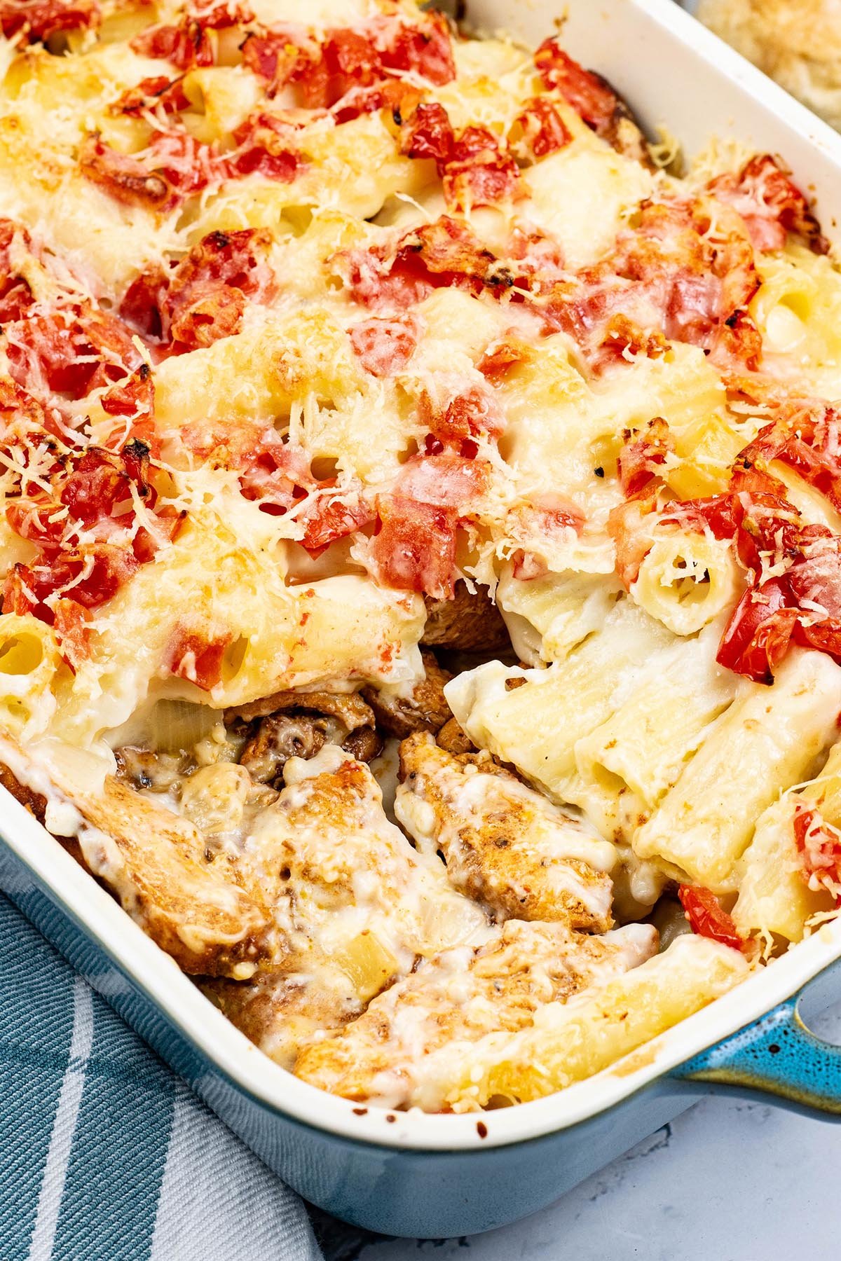 Chicken pasta bake in a rectangle Staub ovenproof dish with a teal and white checked towel on the side.