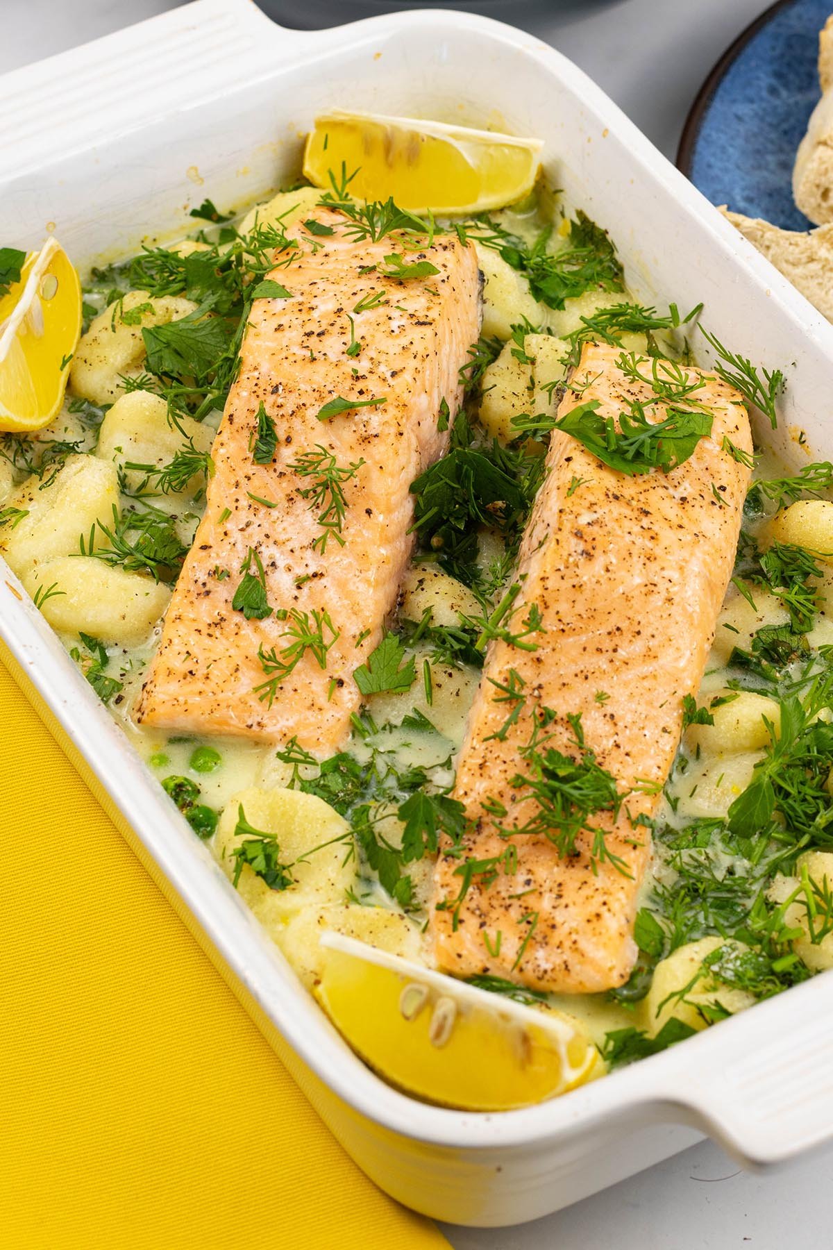 Two portions of salmon with gnocchi, peas and broad beans in a white rectangle oven dish.