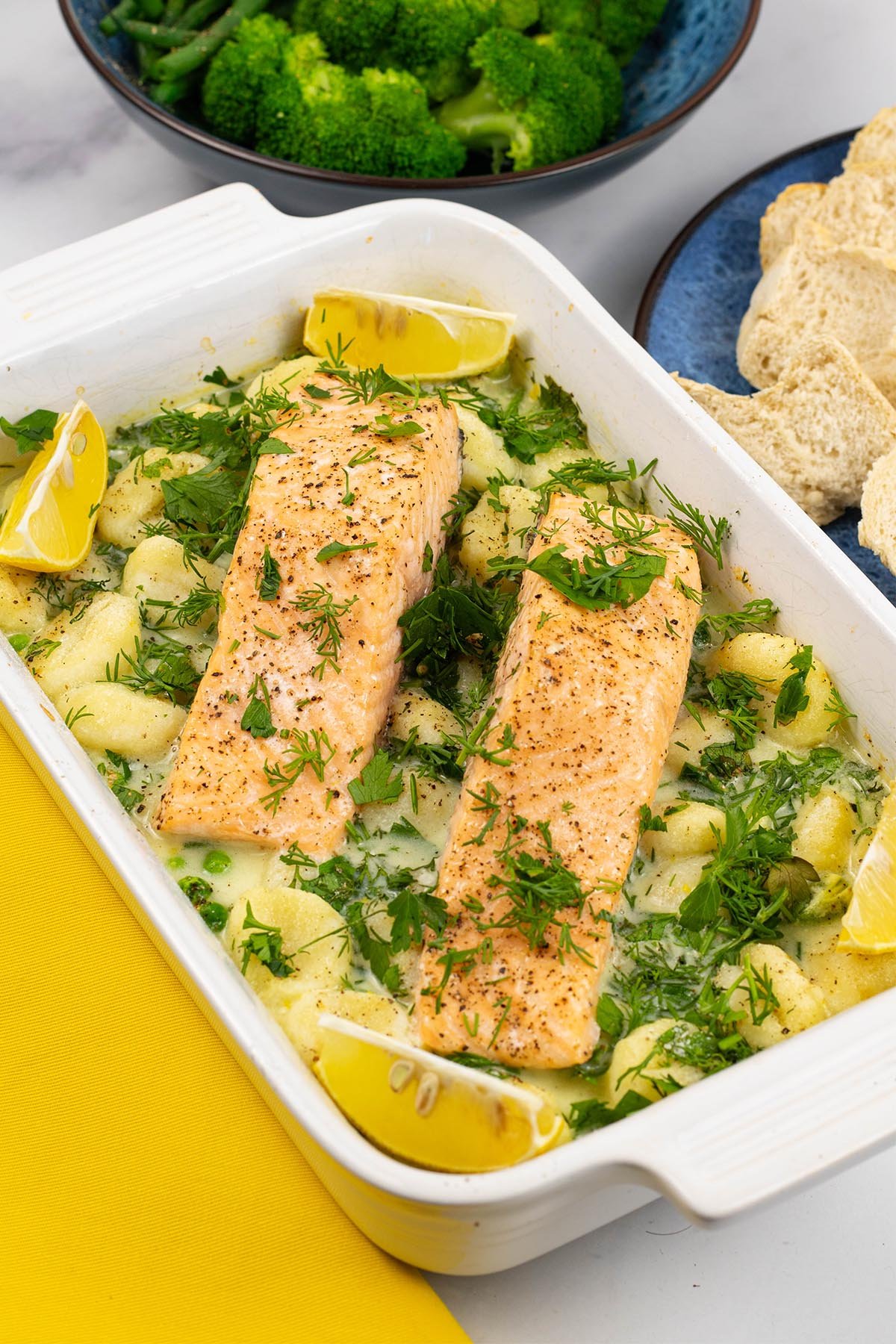 Two portions of salmon with gnocchi, peas and broad beans in a white rectangle oven dish.