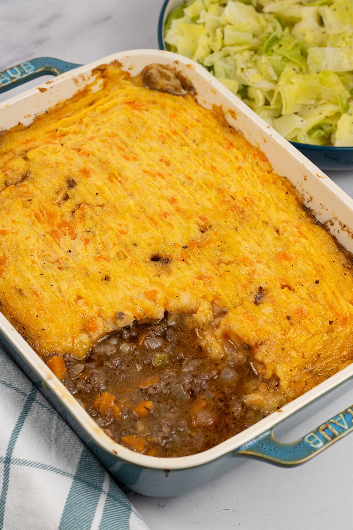 Venison mince pie in a rectangular Staub ovenproof dish with a bowl of easy buttered cabbage on the side.