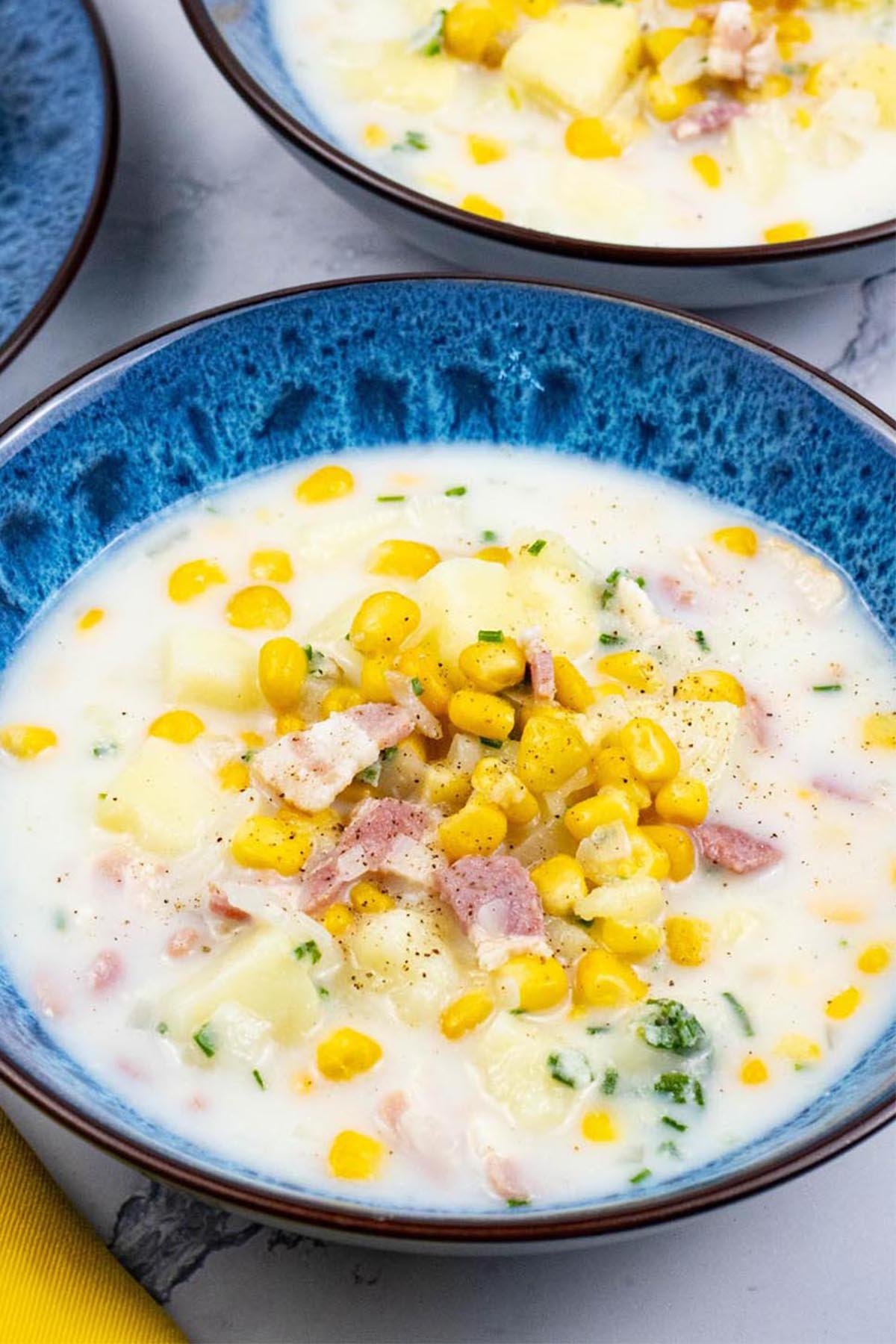Close up of two bowls of bacon and sweetcorn chowder in blue patterned bowls.