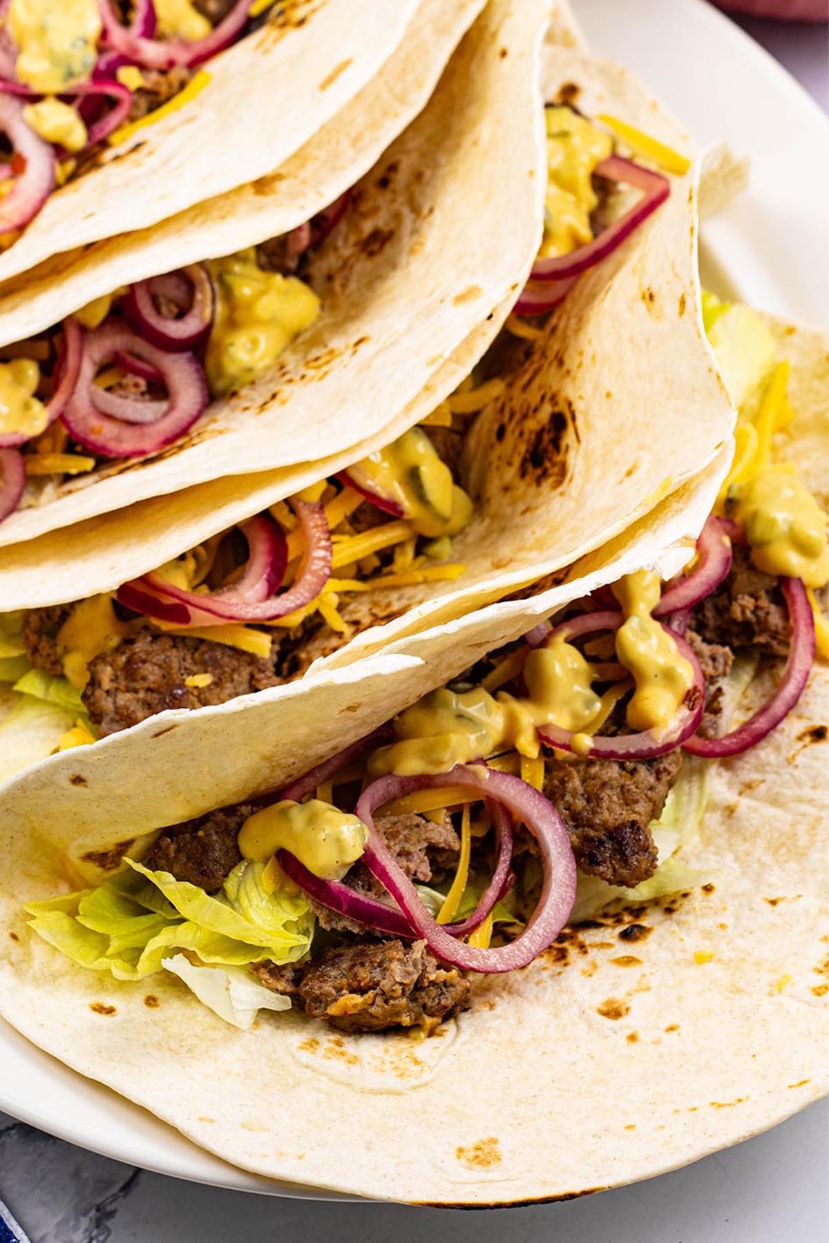 4 cheeseburger tacos on a white oval platter with paper napkins on the side.