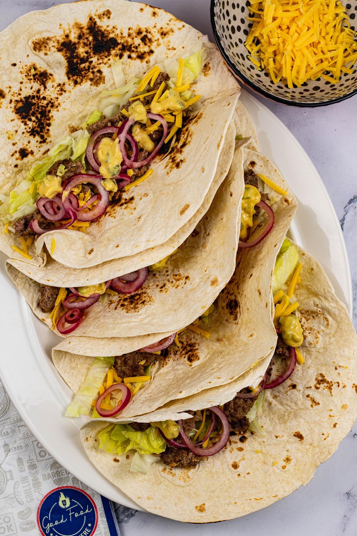 4 cheeseburger tacos on a white oval platter with paper napkins on the side.