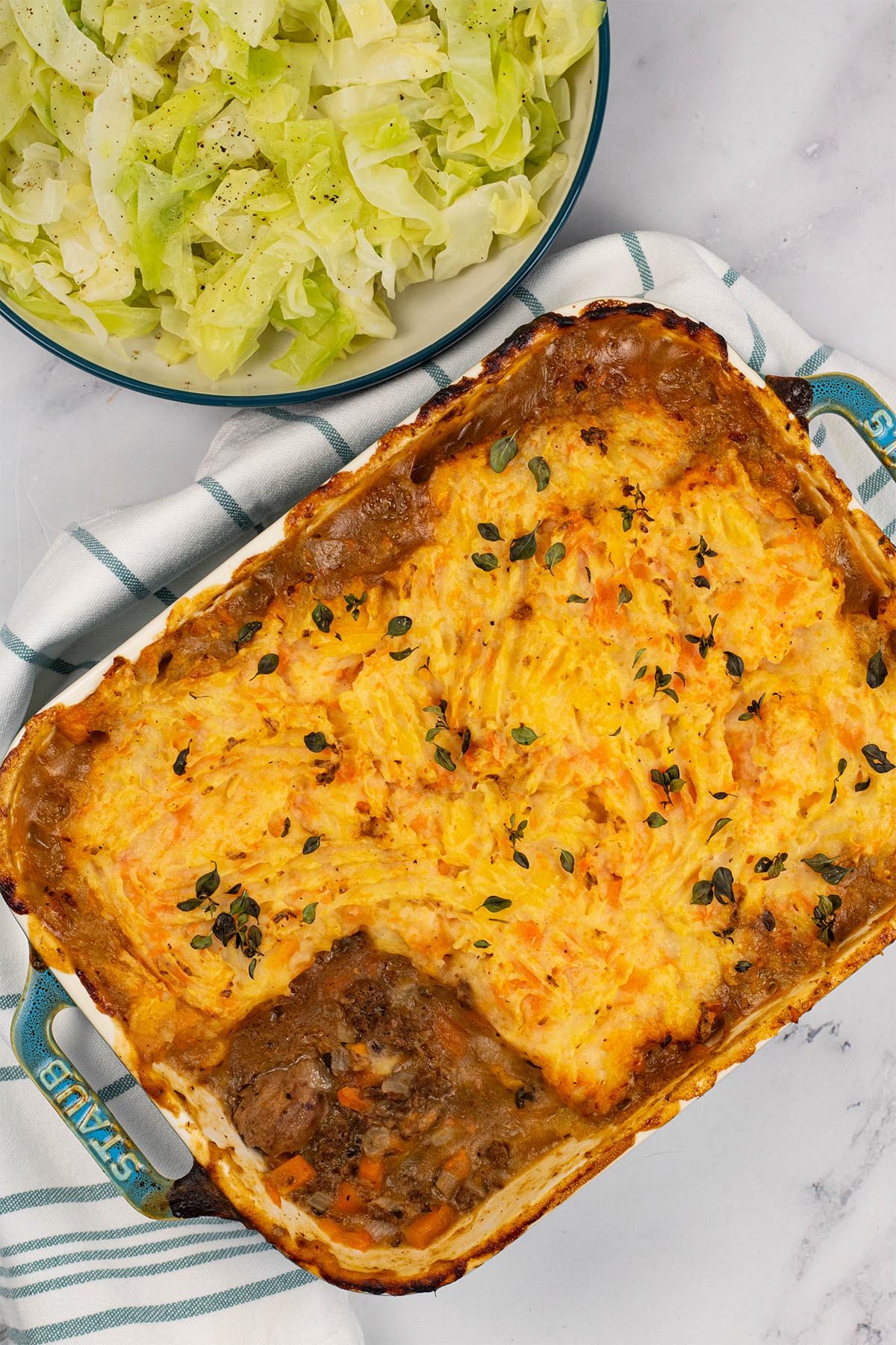 Gamekeeper's pie in a rectangular Staub ovenproof dish with a bowl of buttered cabbage on the side.