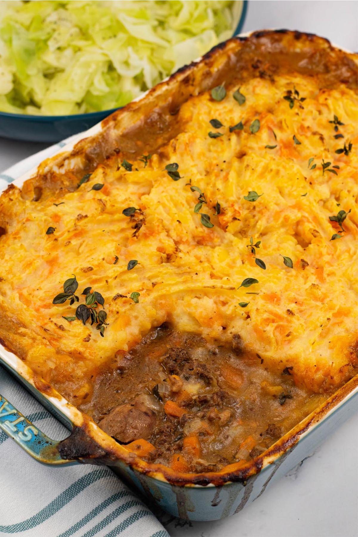 Gamekeeper's pie in a rectangular Staub ovenproof dish with a bowl of buttered cabbage on the side.