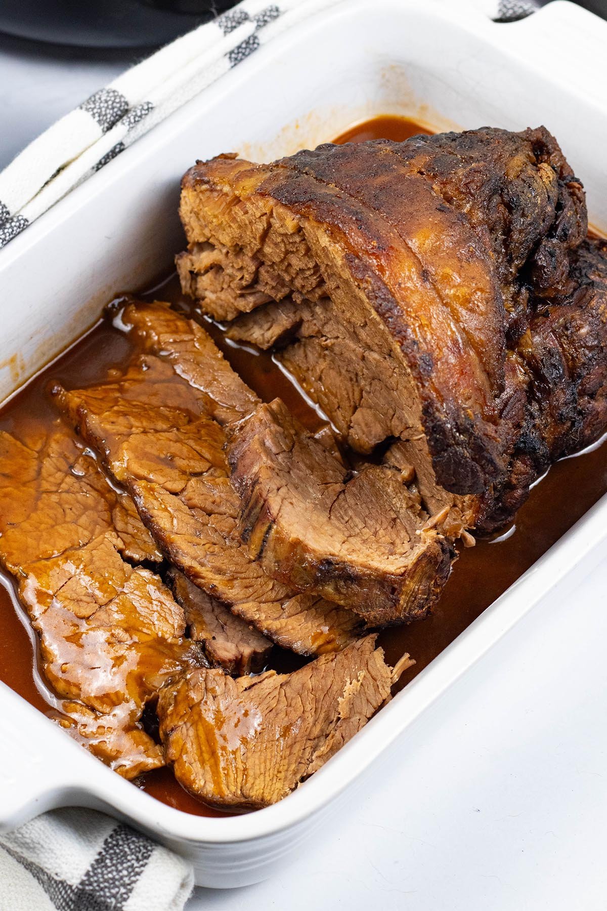 Slow cooker beef pot roast sitting in a white rectangular serving dish with gravy and a couple of slices carved.