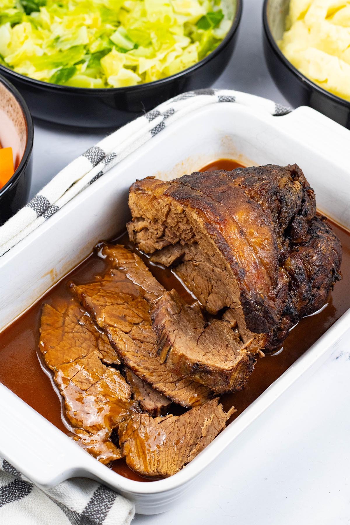 Slow cooker beef pot roast sitting in a white rectangular serving dish with gravy and a couple of slices carved.