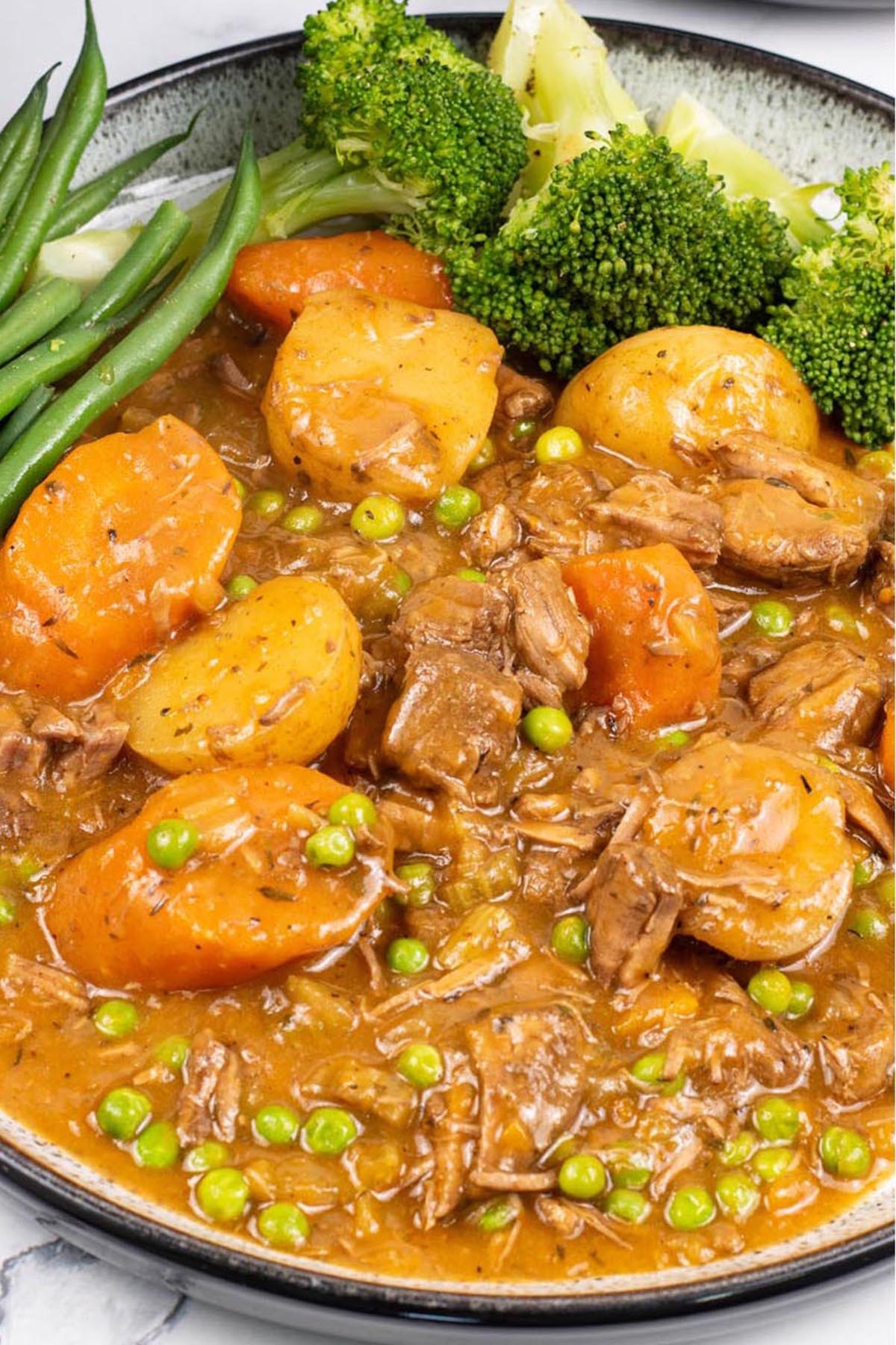 A portion of slow cooker old fashioned beef stew on a black and white patterned dinner plate with broccoli and green beans on the side.