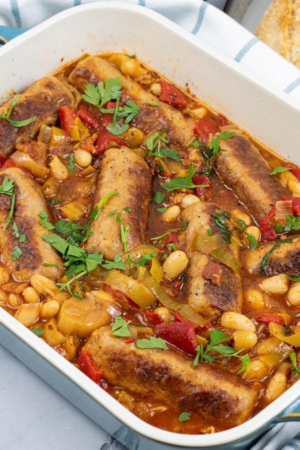 Slow cooker sausage casserole in a rectangle Staub serving dish with a baguette in the background.