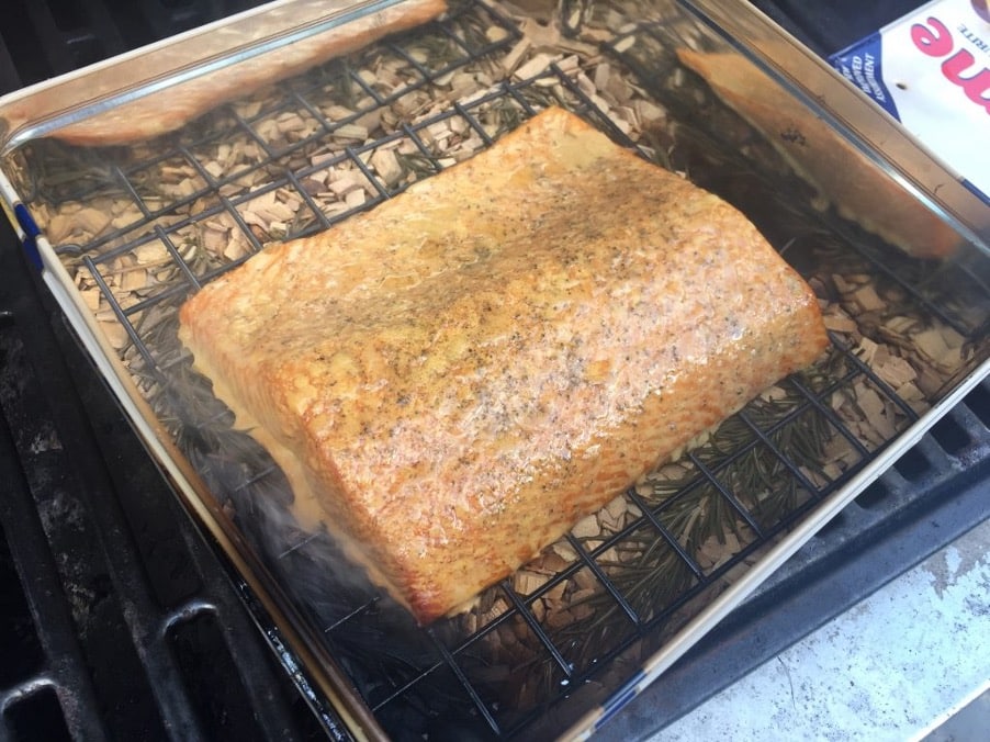 Half side of salmon in a biscuit tin with rosemary on BBQ