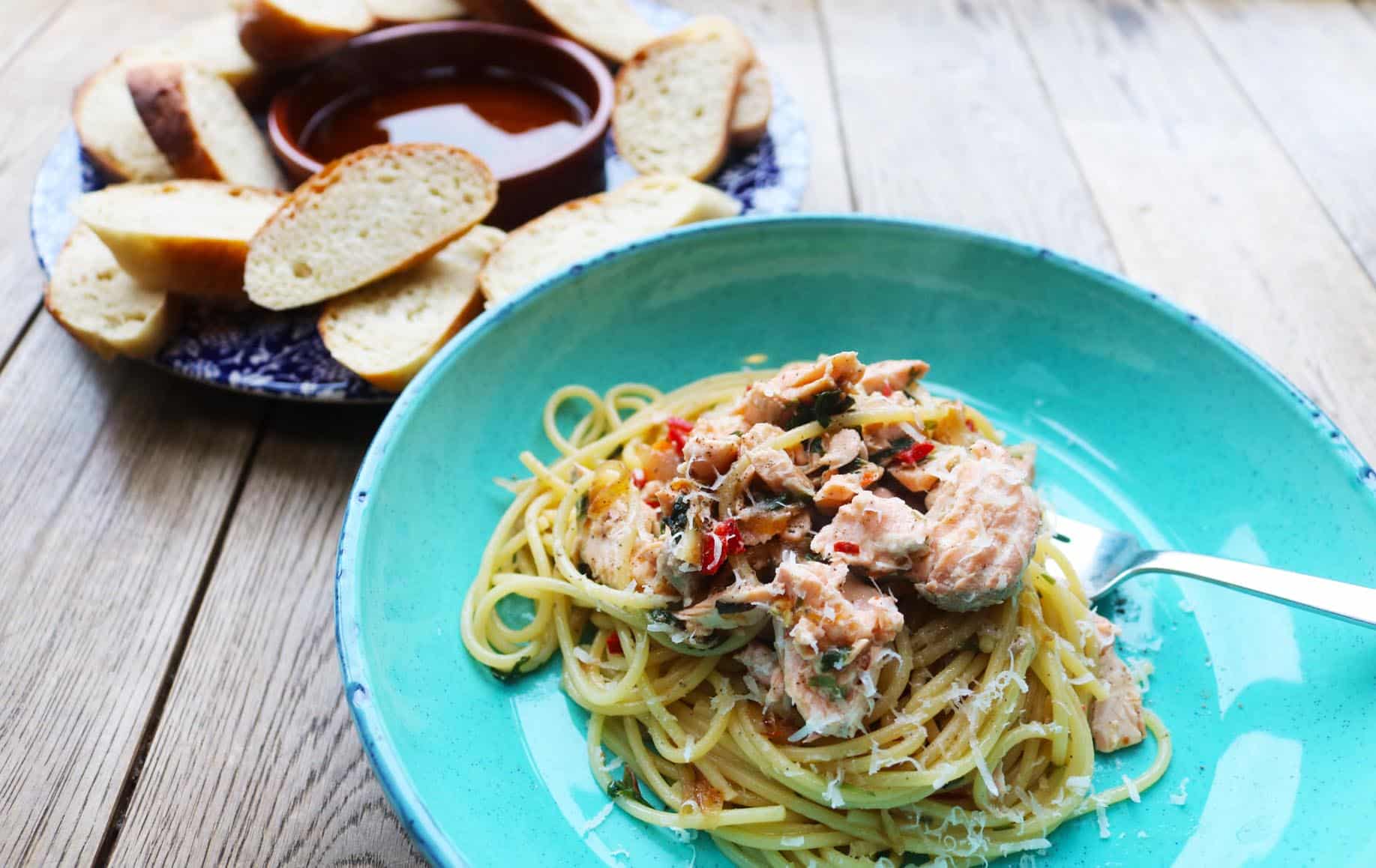Spaghetti and salmon served in a turquoise blue pasta bowl with bread and oil on a plate on the side