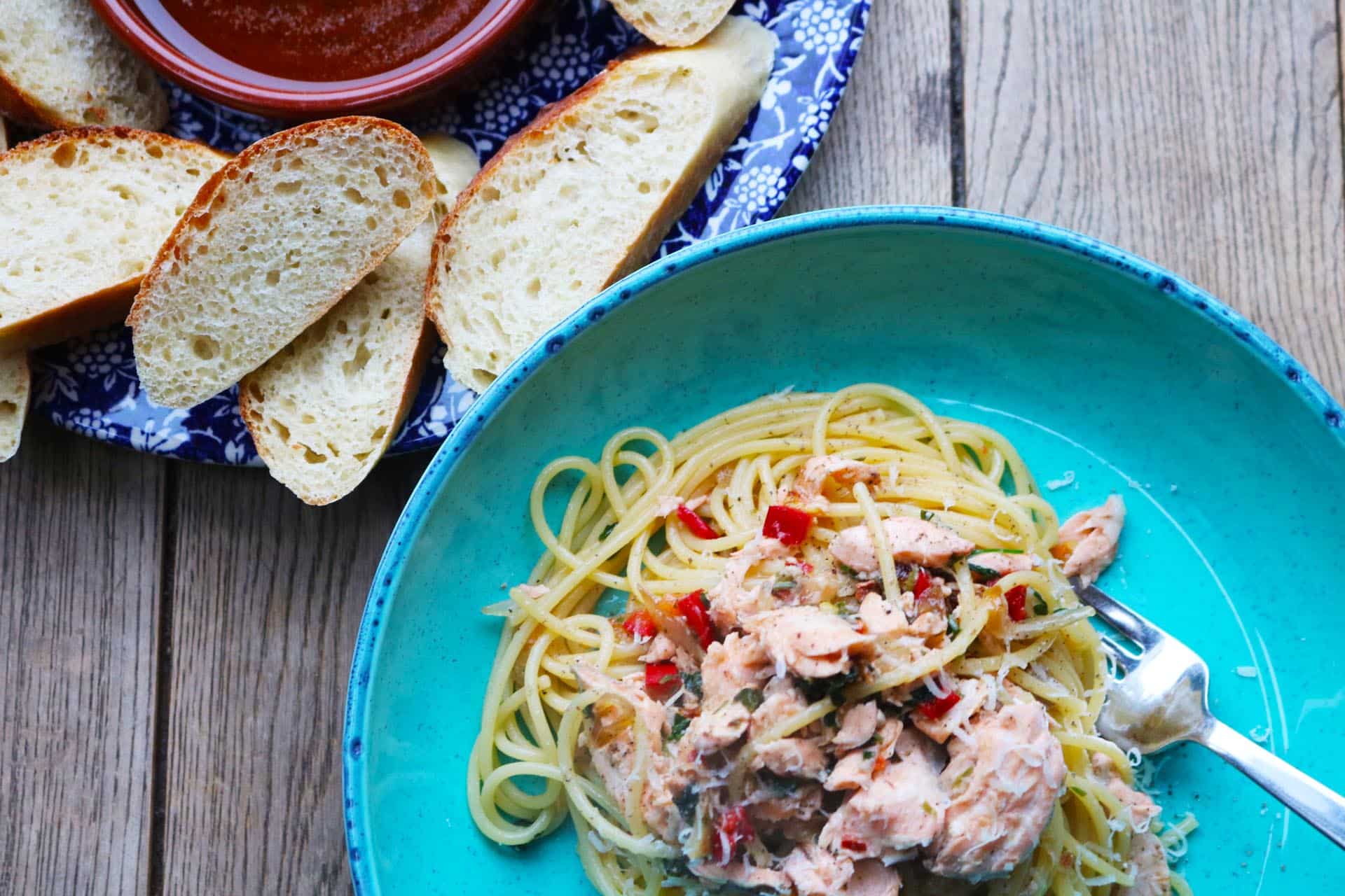 Spaghetti and salmon served in a turquoise blue pasta bowl with bread and oil on a plate on the side