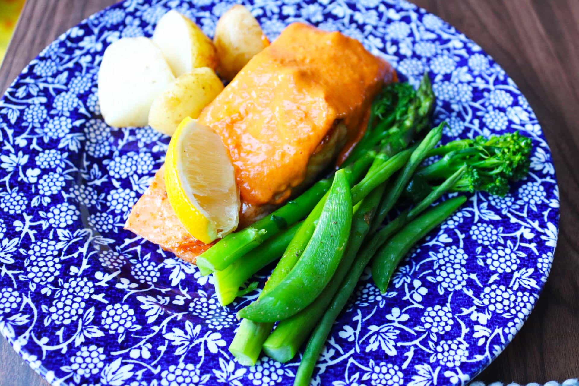Salmon fillet dressed with the hollandaise on a blue and white dinner plate with green veg and new potatoes